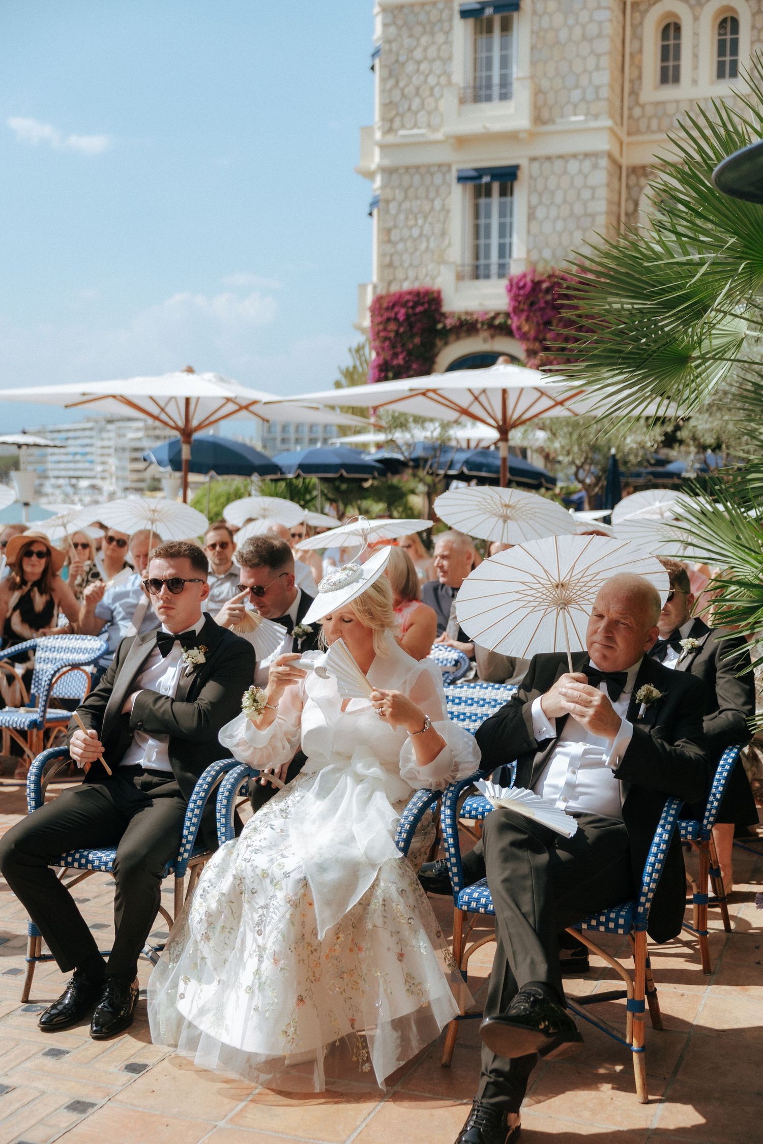 Wedding guests seated under white parasols at an elegant outdoor Mediterranean venue.