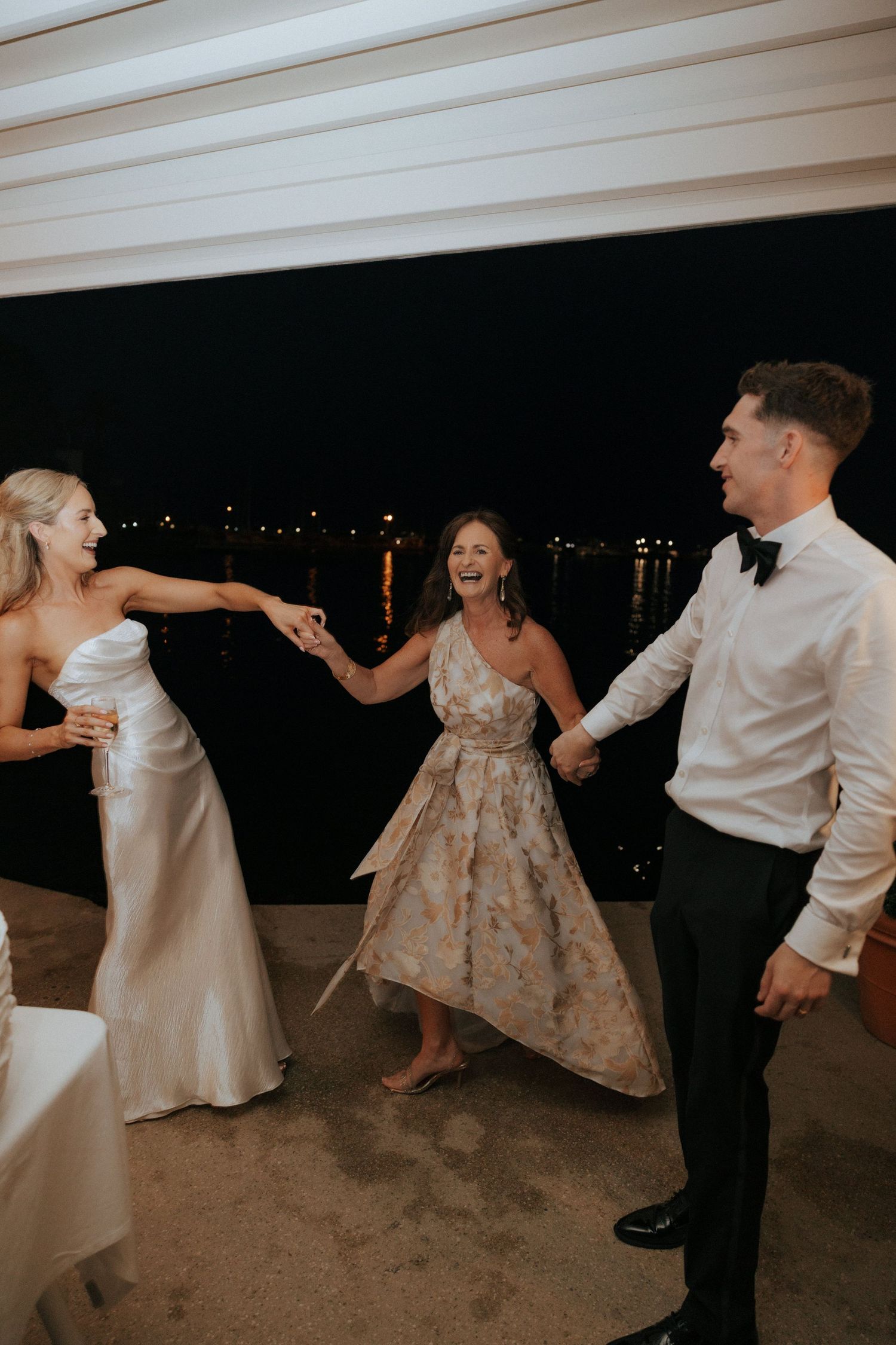Wedding party dancing and celebrating at evening reception under white ceiling.