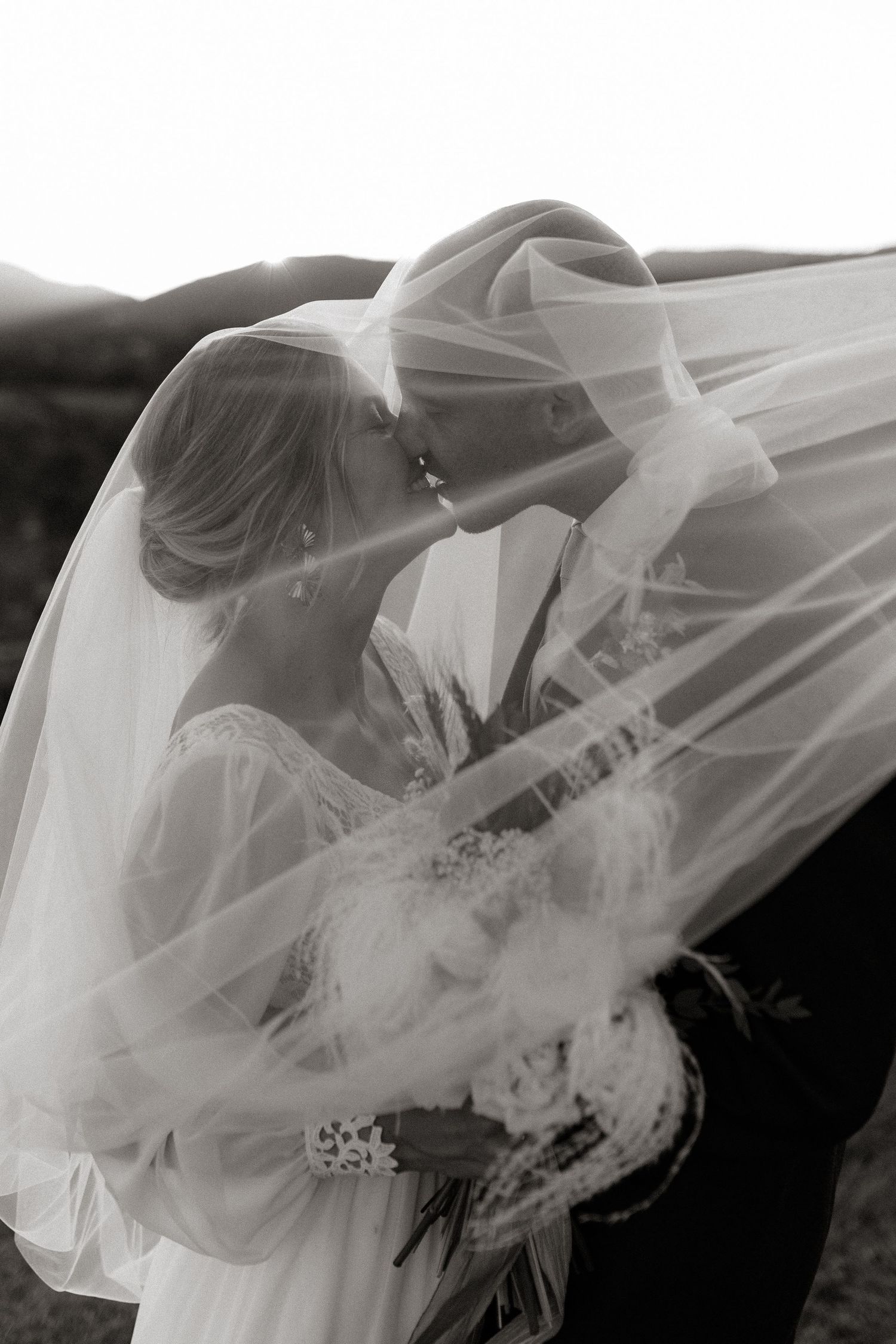 Black and white photo of romantic moment under flowing bridal veil.
