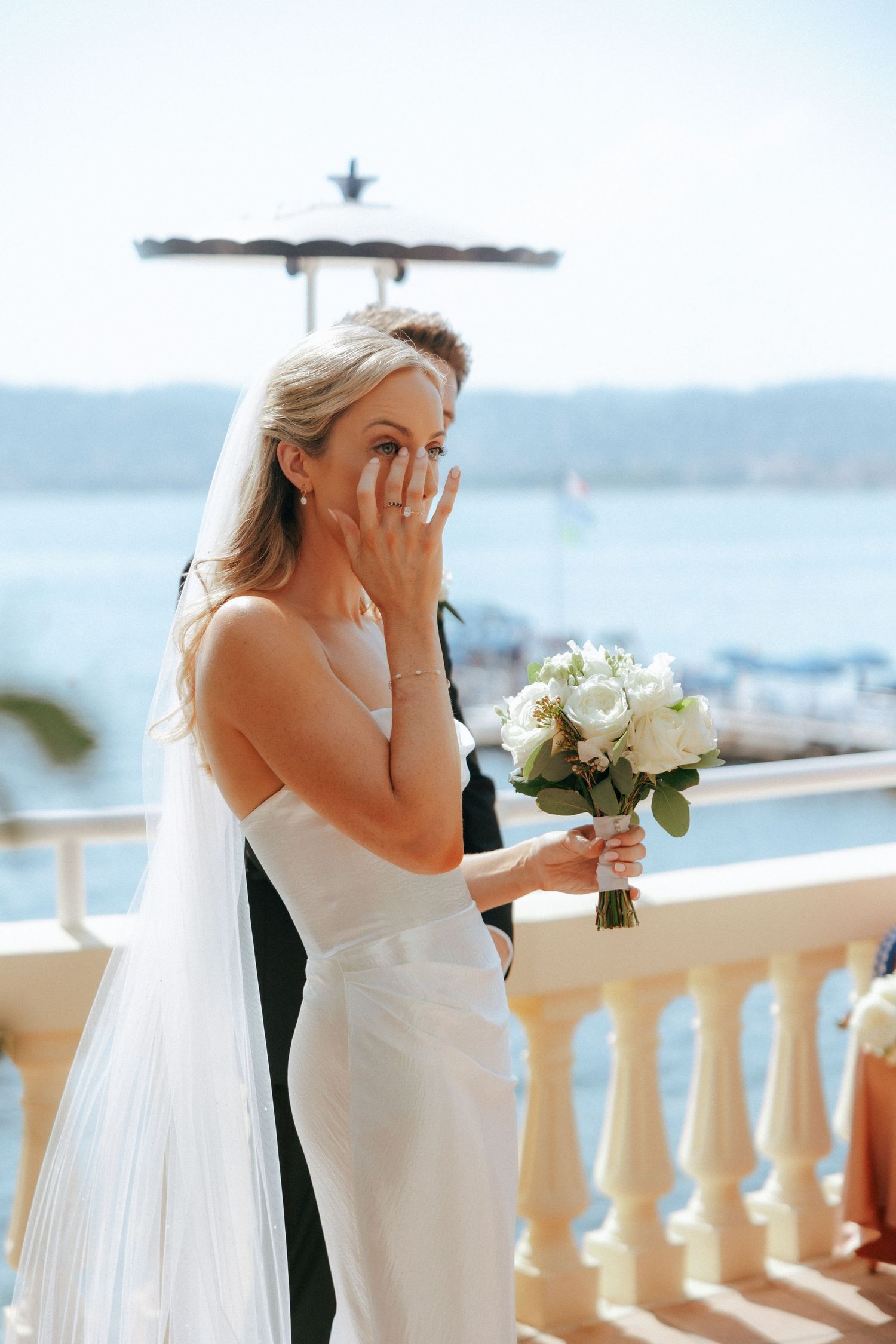 Emotional wedding moment captured on Mediterranean balcony overlooking ocean vista.