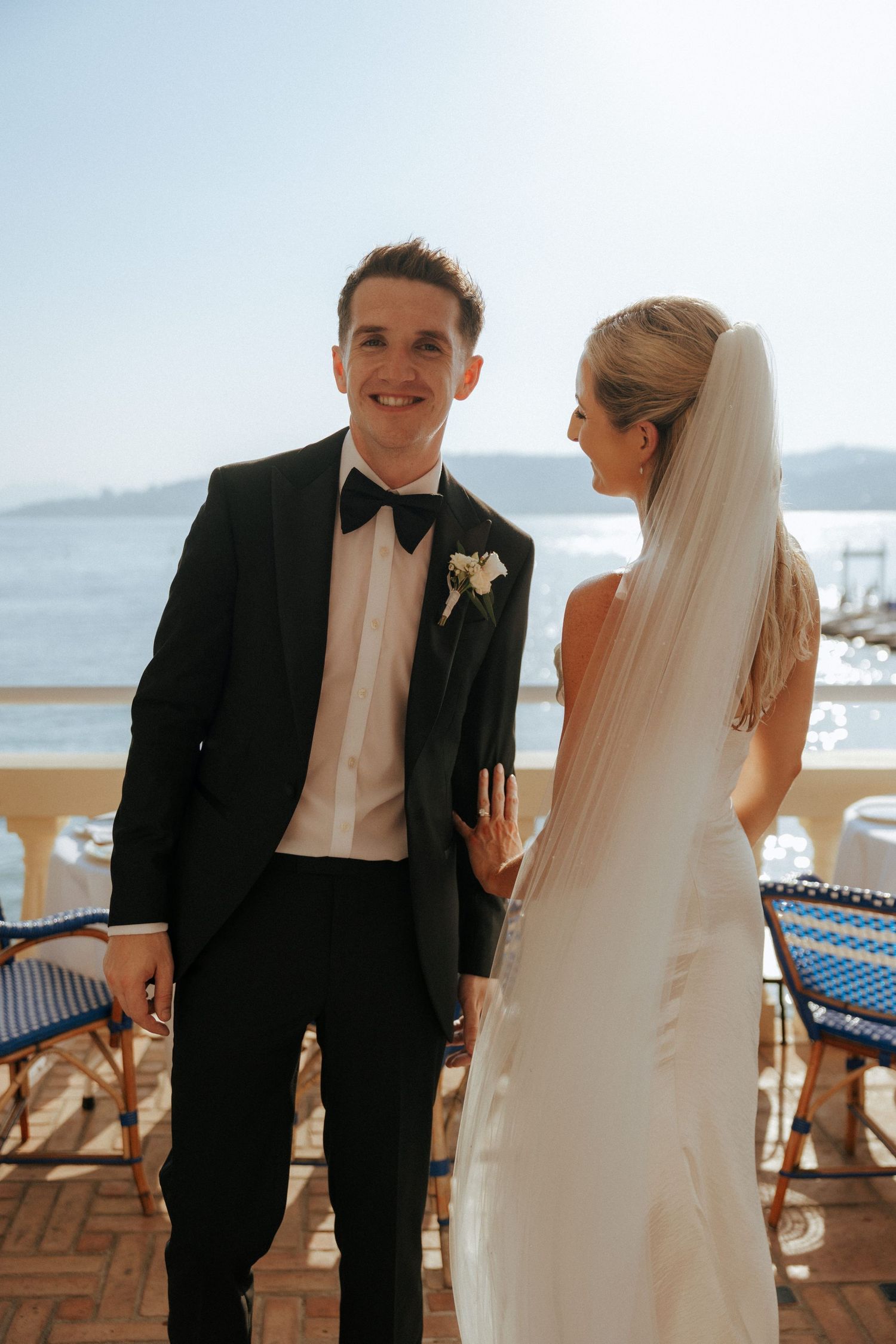 Bride and groom share intimate moments on a waterfront terrace during their wedding celebration.