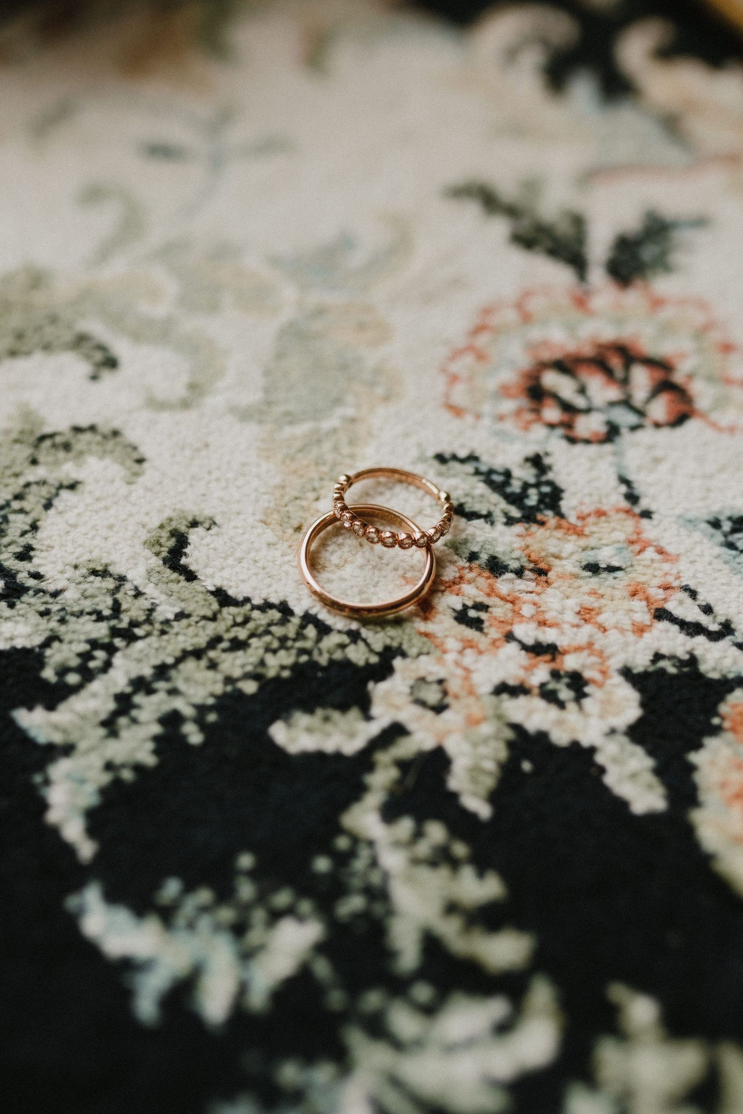 Two gold wedding rings rest on a floral black and white patterned fabric with coral accents.