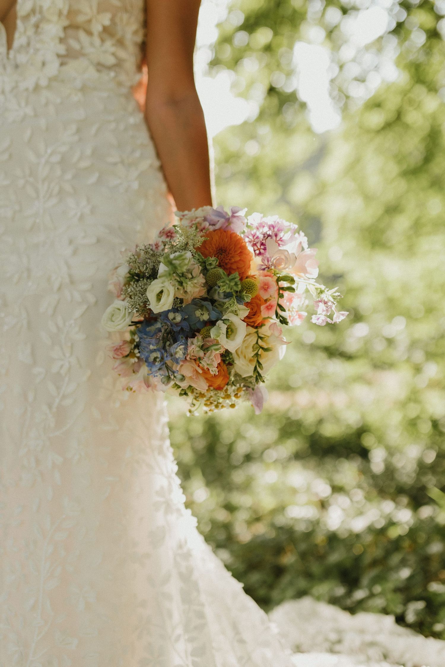 Delicate bridal bouquet with pastel flowers and greenery held against a white lace wedding dress.