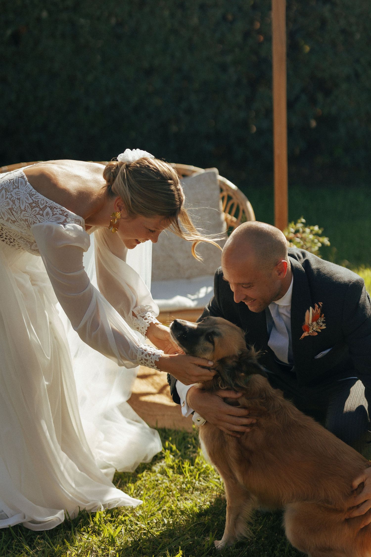 A couple in wedding attire petting their dog during their outdoor ceremony.