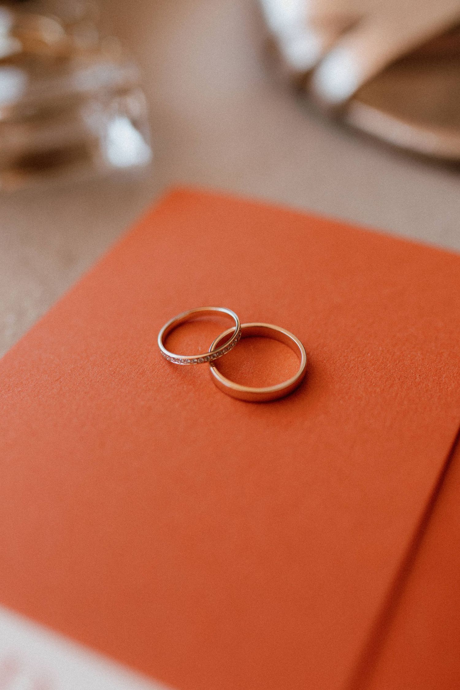 Two wedding rings resting on coral orange notebook or invitation showing delicate details.