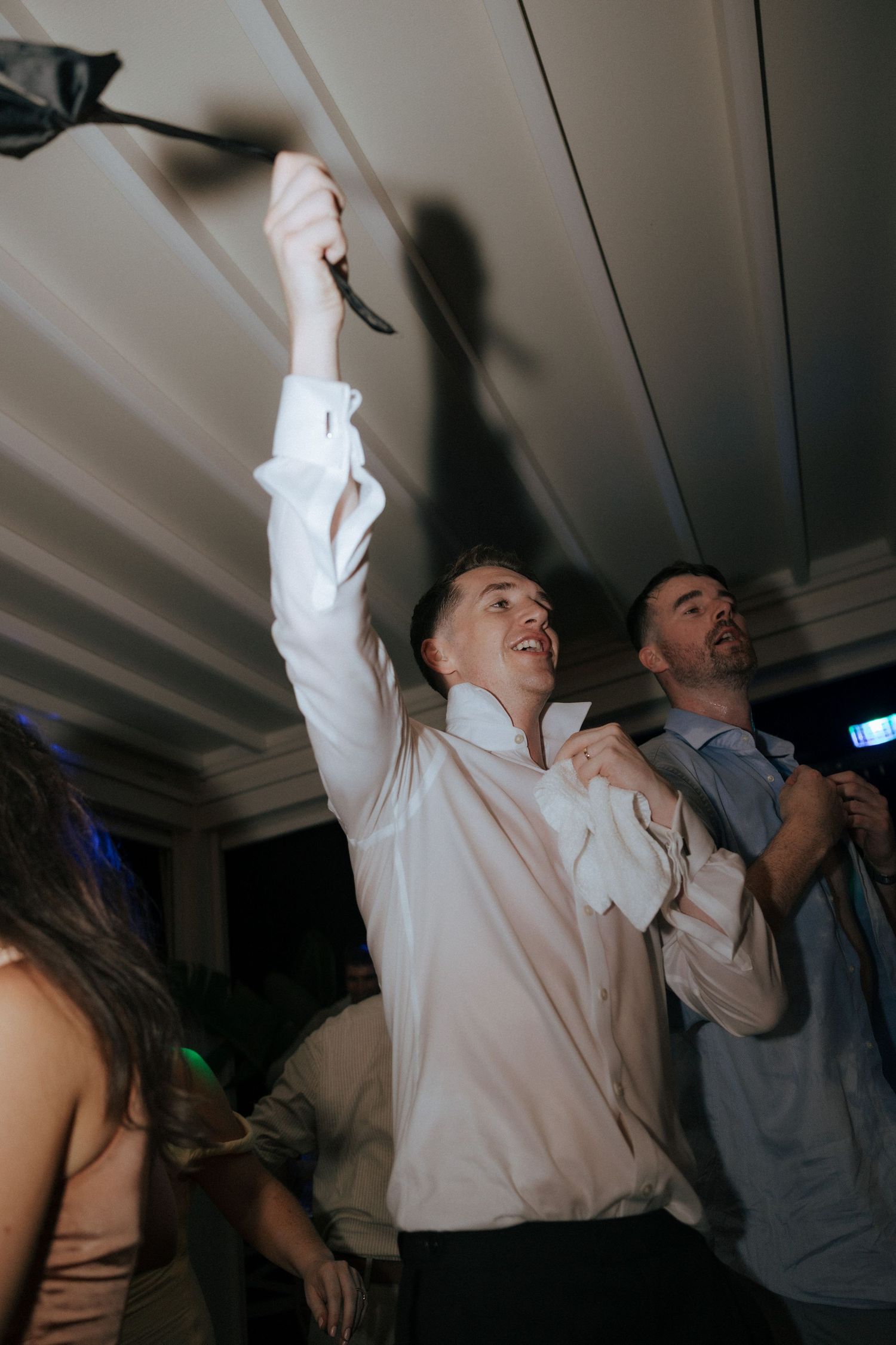 Wedding reception party guests dancing and celebrating in a dimly lit venue.