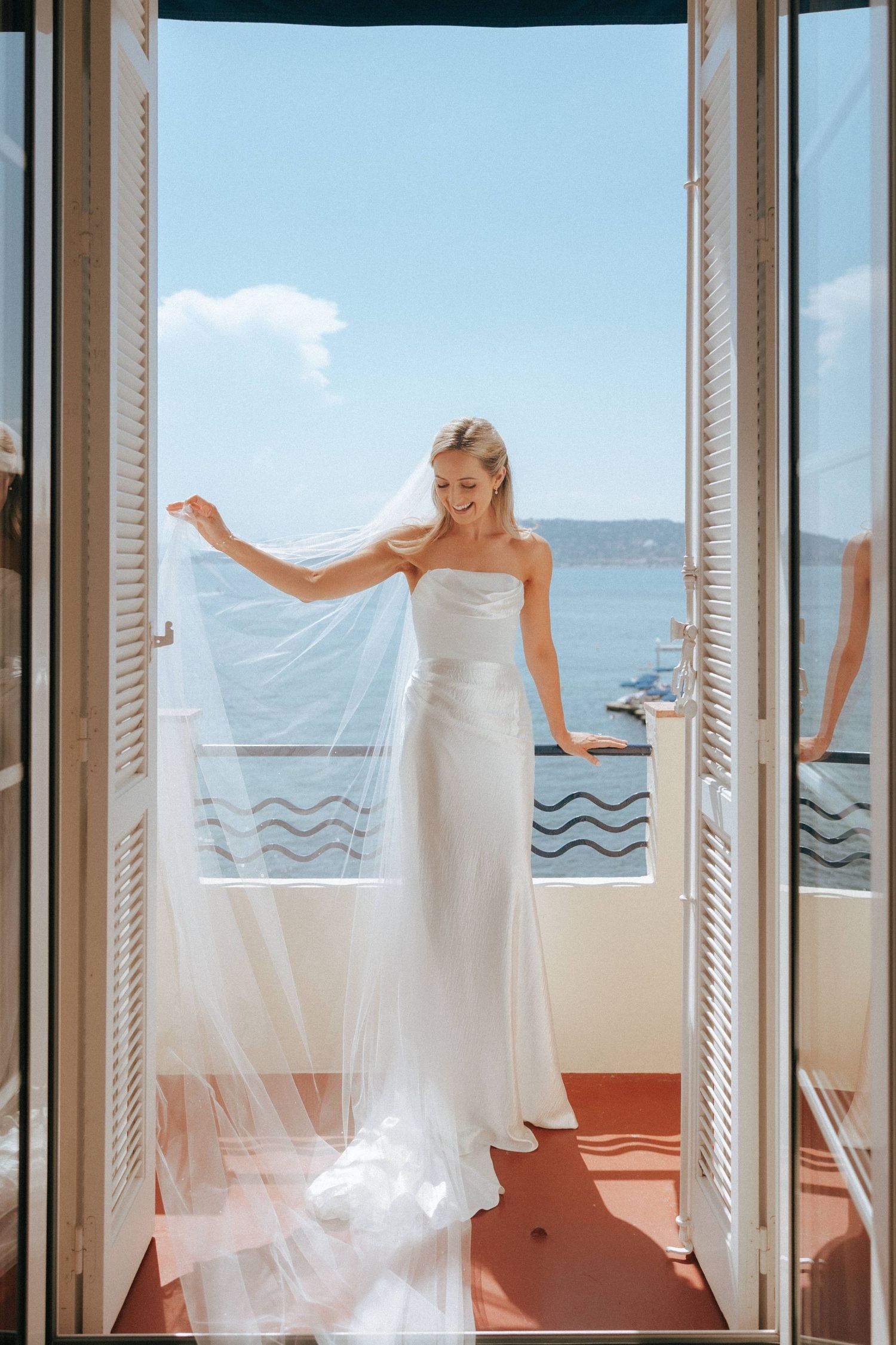 A white wedding dress flowing in the breeze on a sunlit balcony overlooking the ocean.
