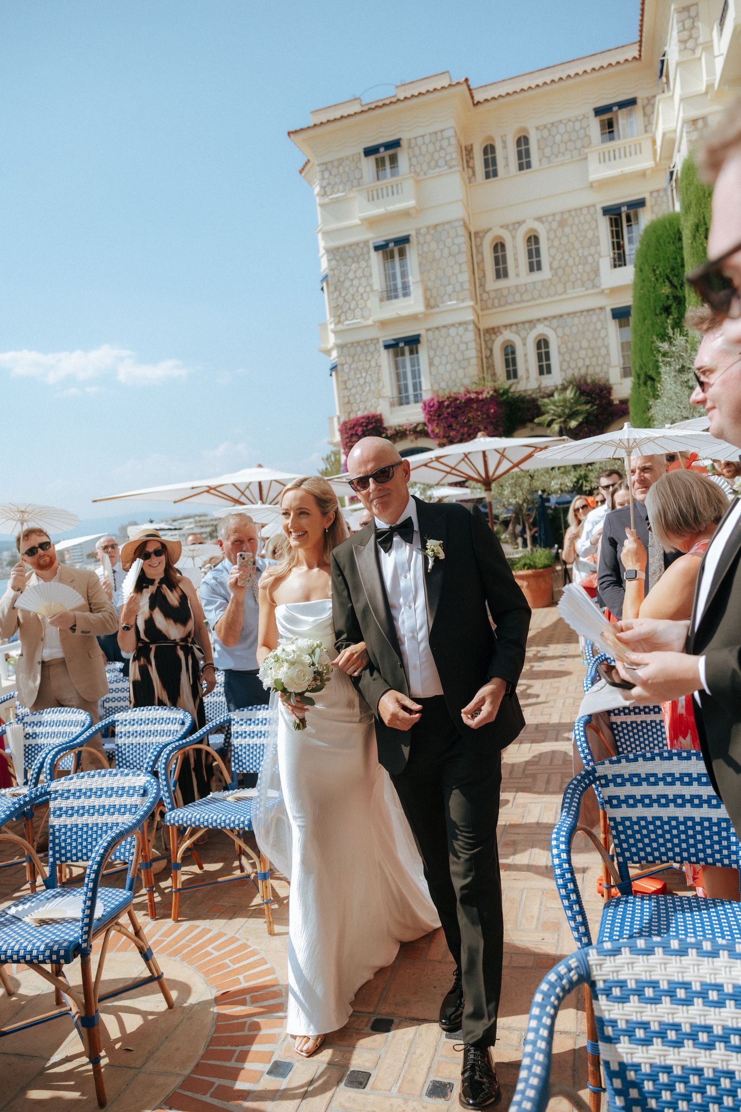 Outdoor wedding reception scene with elegant table settings and parasols on a sunny coastal patio.