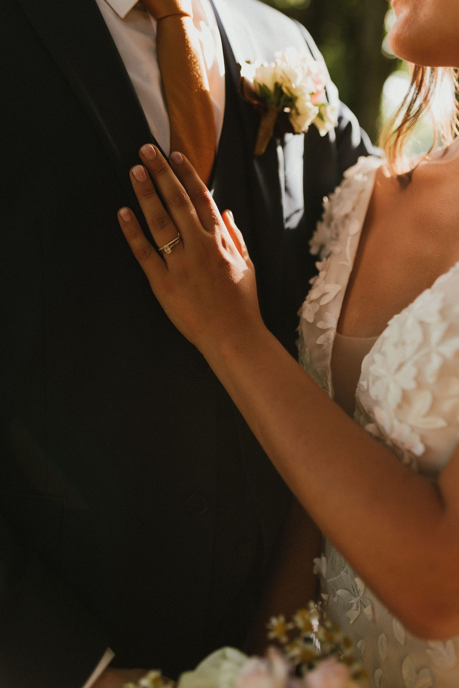 Close-up of hands showing wedding rings against formal attire in warm sunlight.