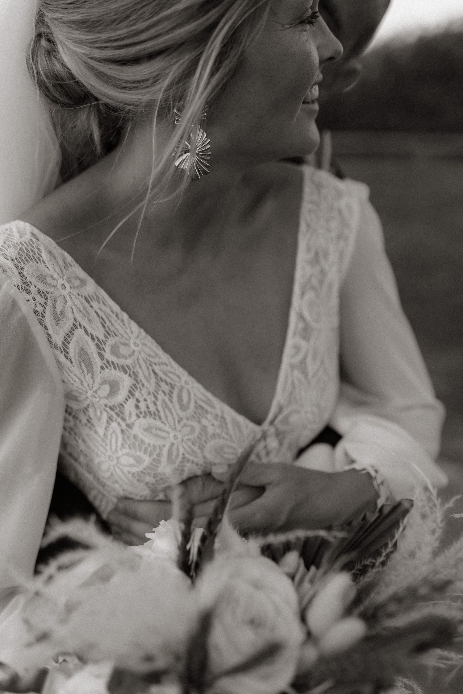 Close up black and white portrait of bride wearing delicate lace dress with detailed neckline and floral bouquet.