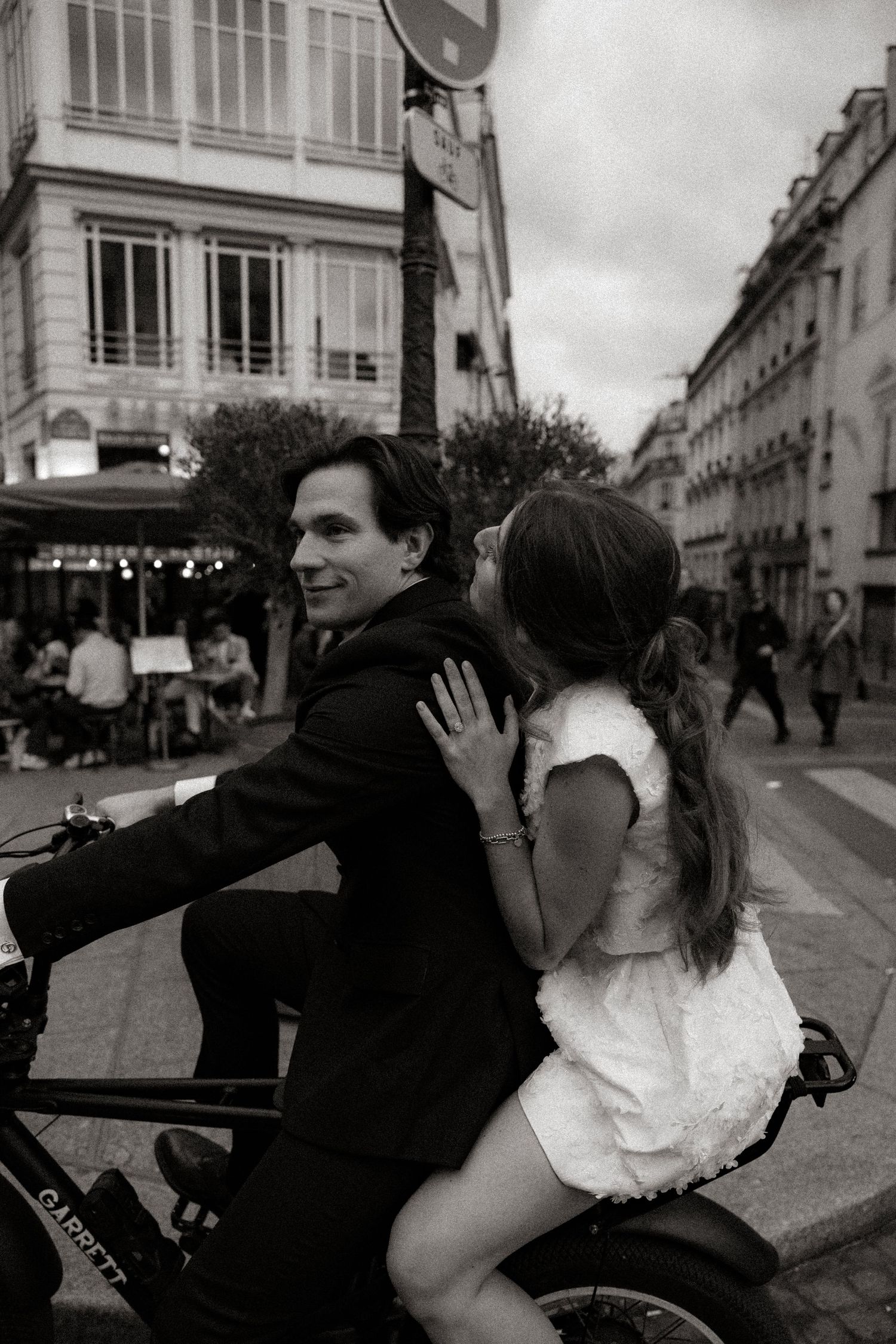 A romantic black and white street scene in Paris with a couple sharing a bicycle ride down a charming avenue.