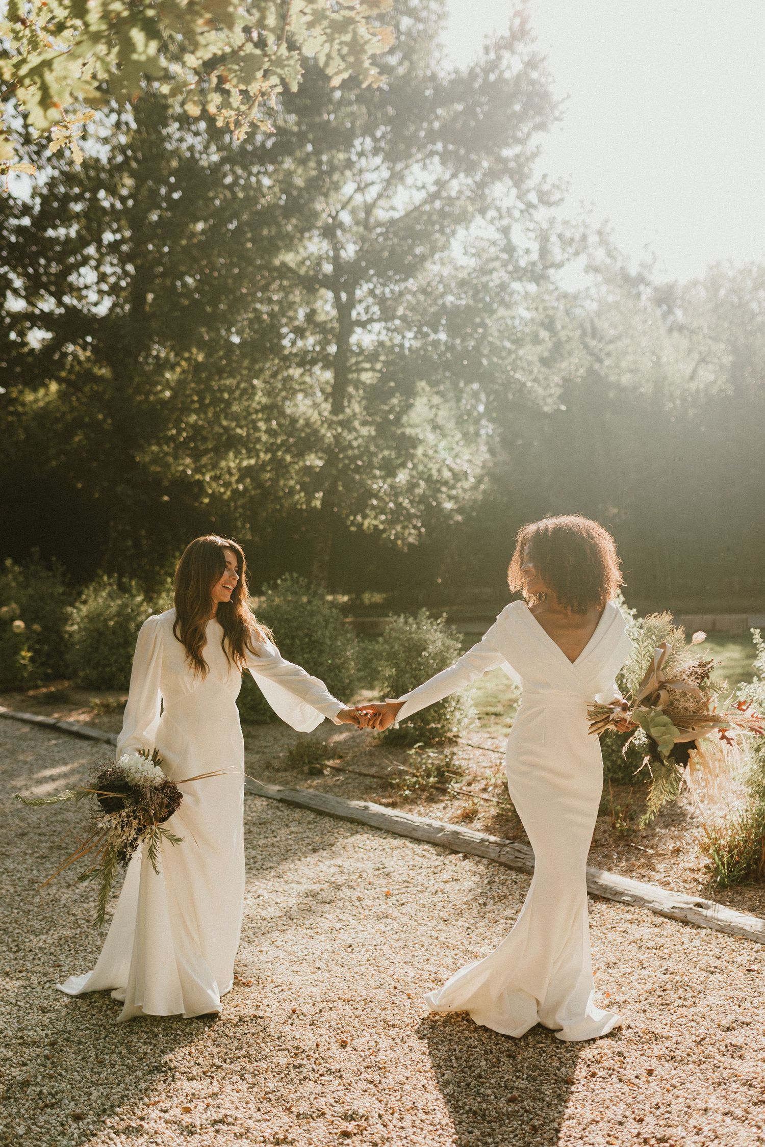 A person in a flowing white dress twirls gracefully in a sun-dappled garden setting at golden hour.