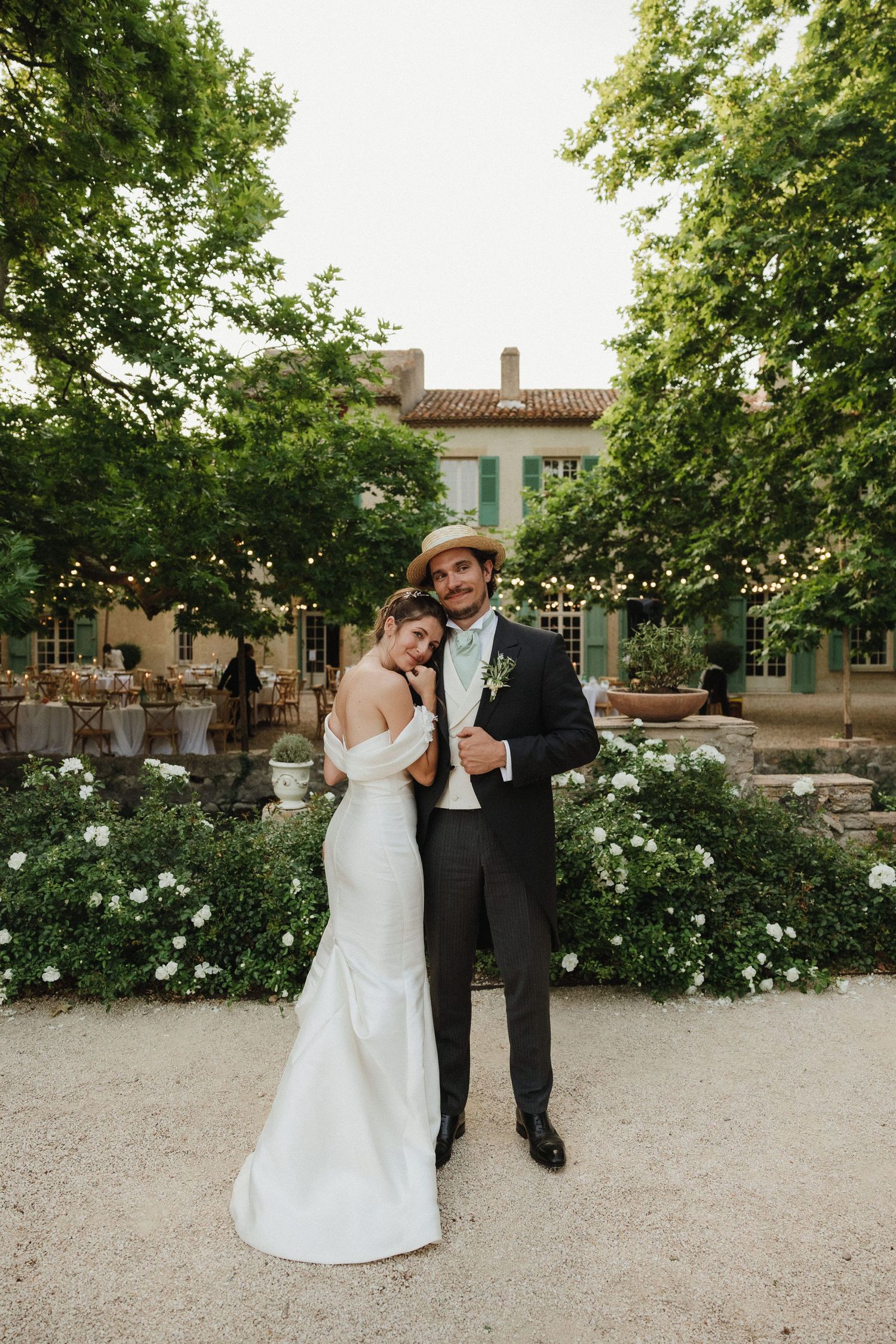 A romantic scene in a garden pathway with white roses where a couple in wedding attire embrace while dancing.