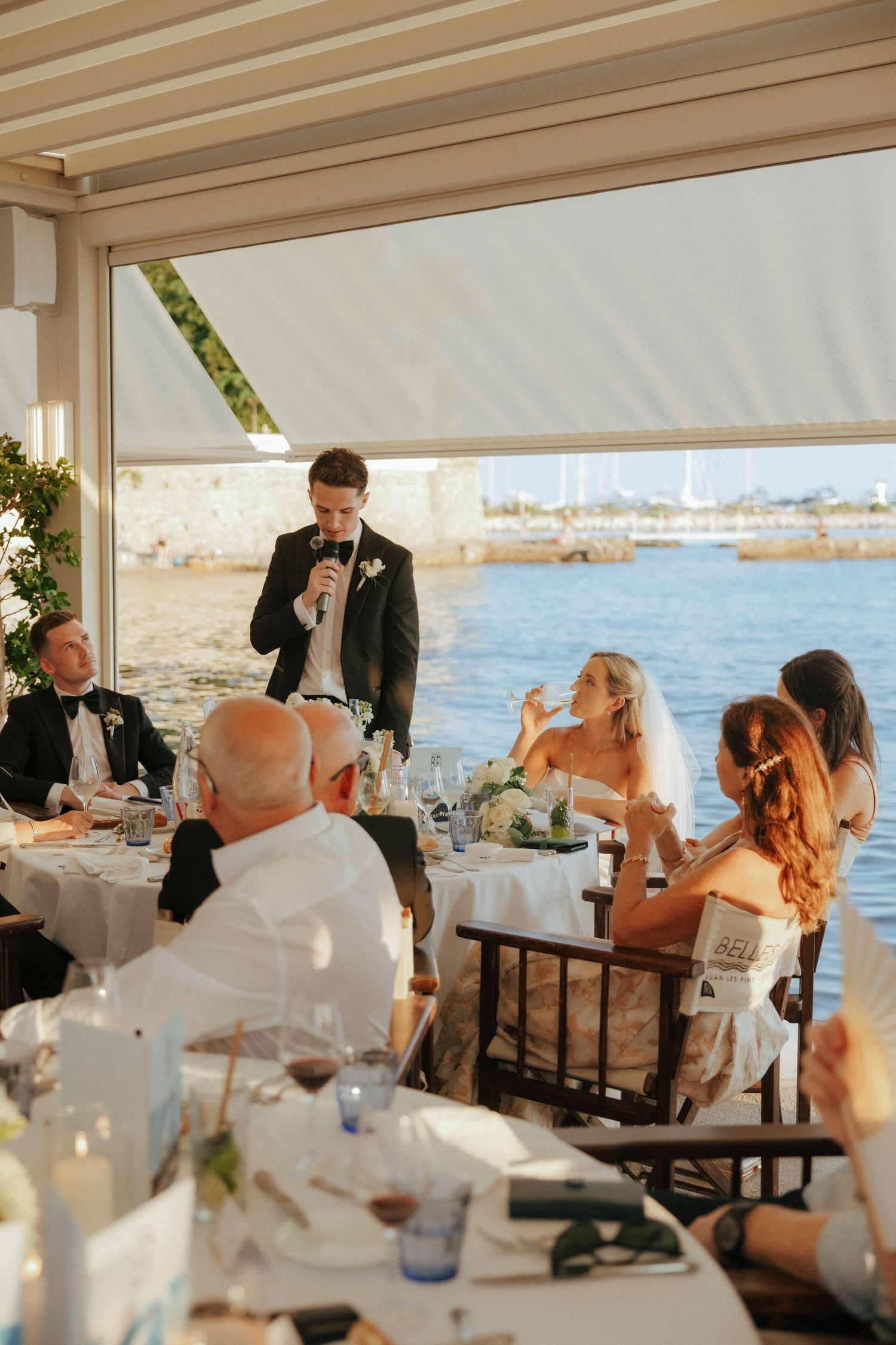 Wedding reception scene at waterfront restaurant with guests dining under covered patio.