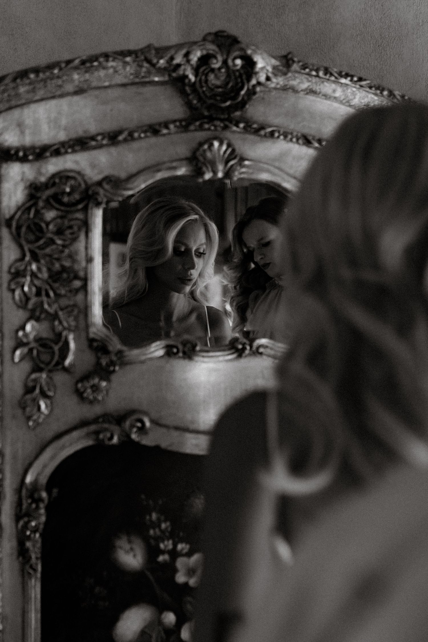 A vintage ornate mirror reflects a silhouette holding a lit cigarette in moody black and white photography.