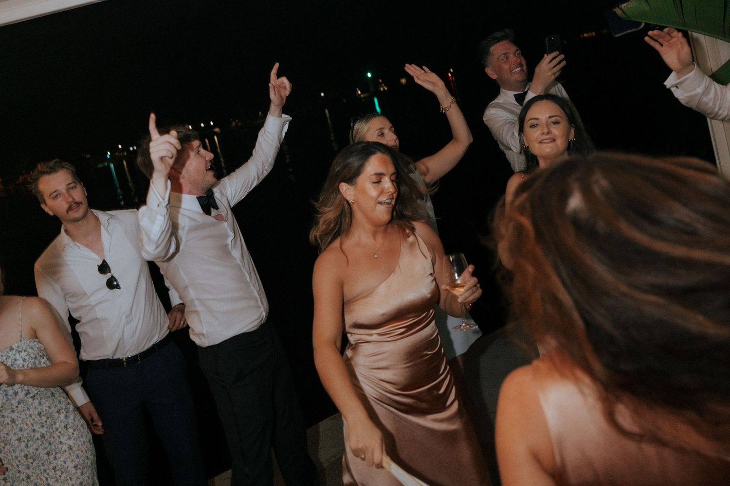 Wedding reception guests dancing together in celebration on a dimly lit dance floor during an evening party.