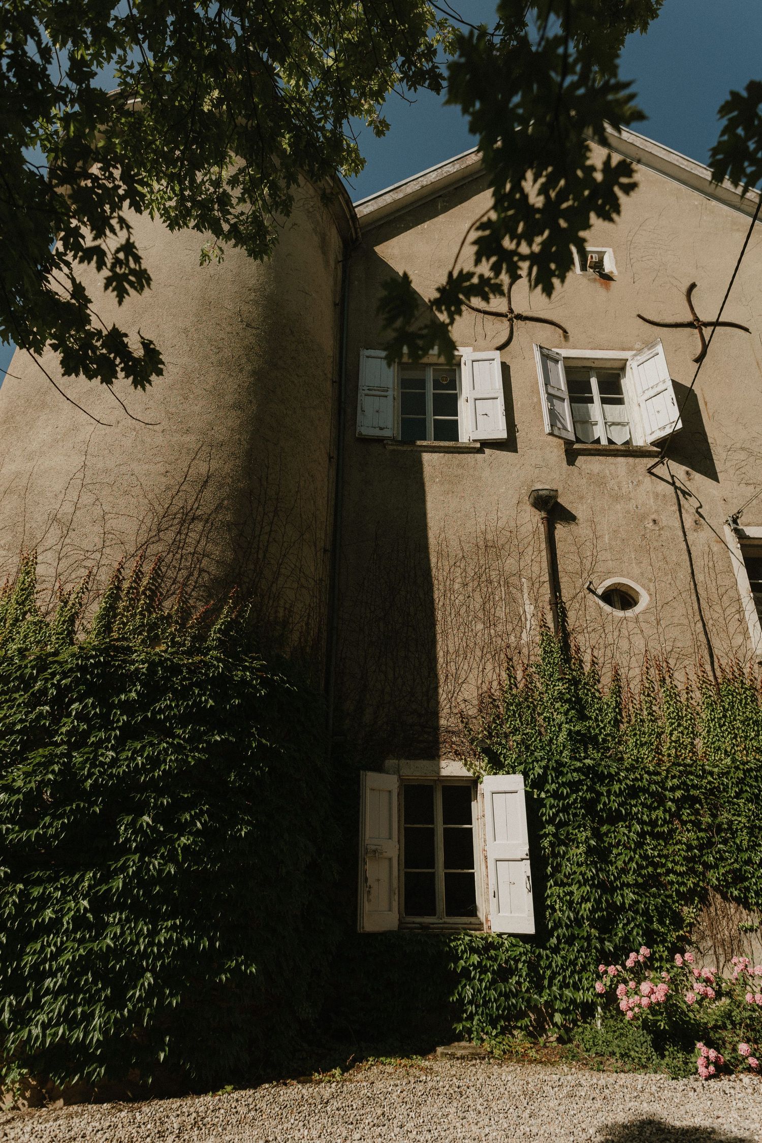 Rustic stone house exterior with white shuttered windows and climbing vines against a moody sky.