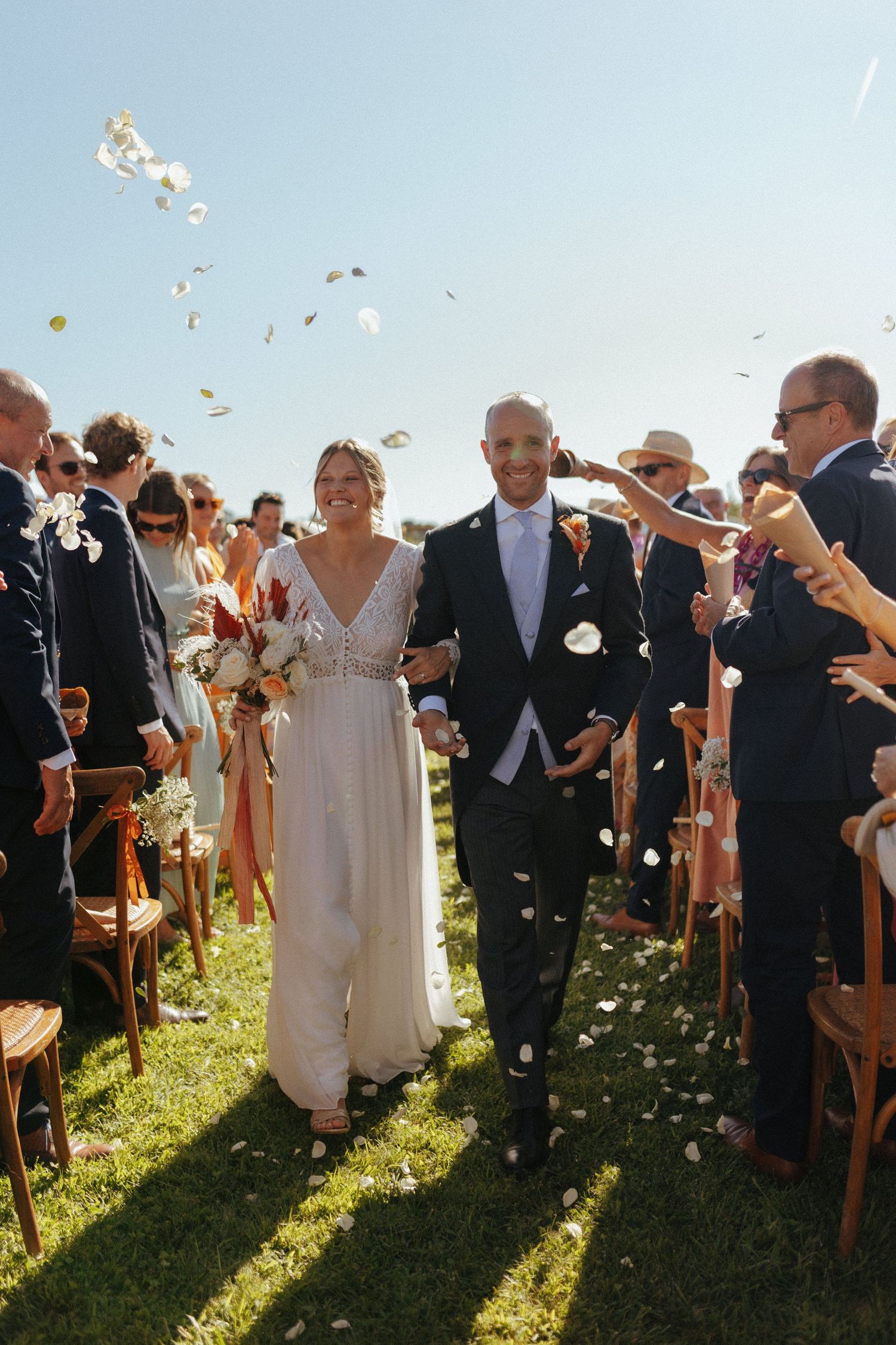 Joyful celebration with floating flower petals as couple walks down aisle at outdoor garden wedding ceremony.