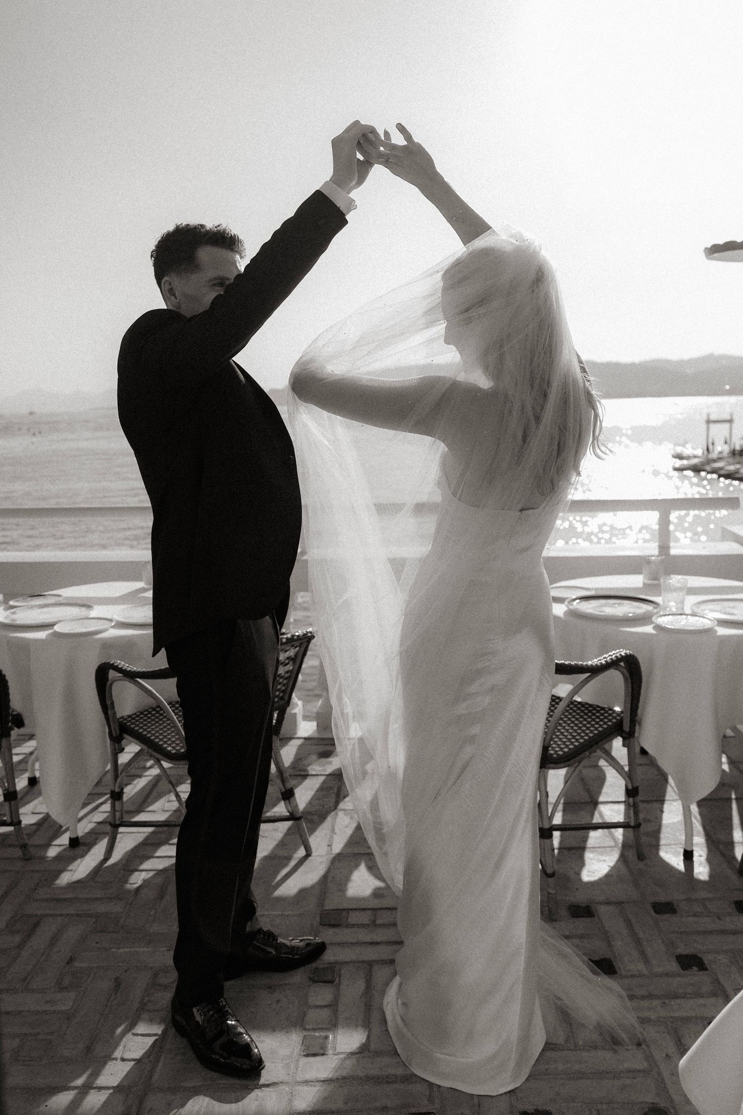A bride and groom dance together on a terrace overlooking the ocean in black and white photography.