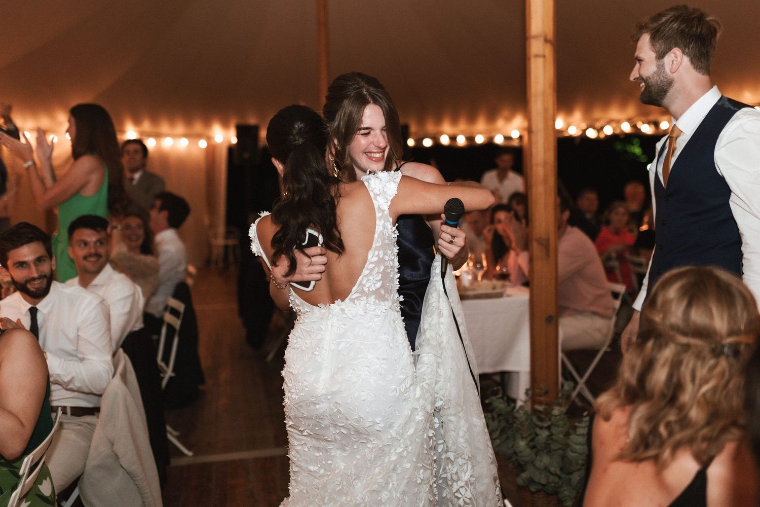 Wedding reception celebration under a tent with dancing and festive lighting.
