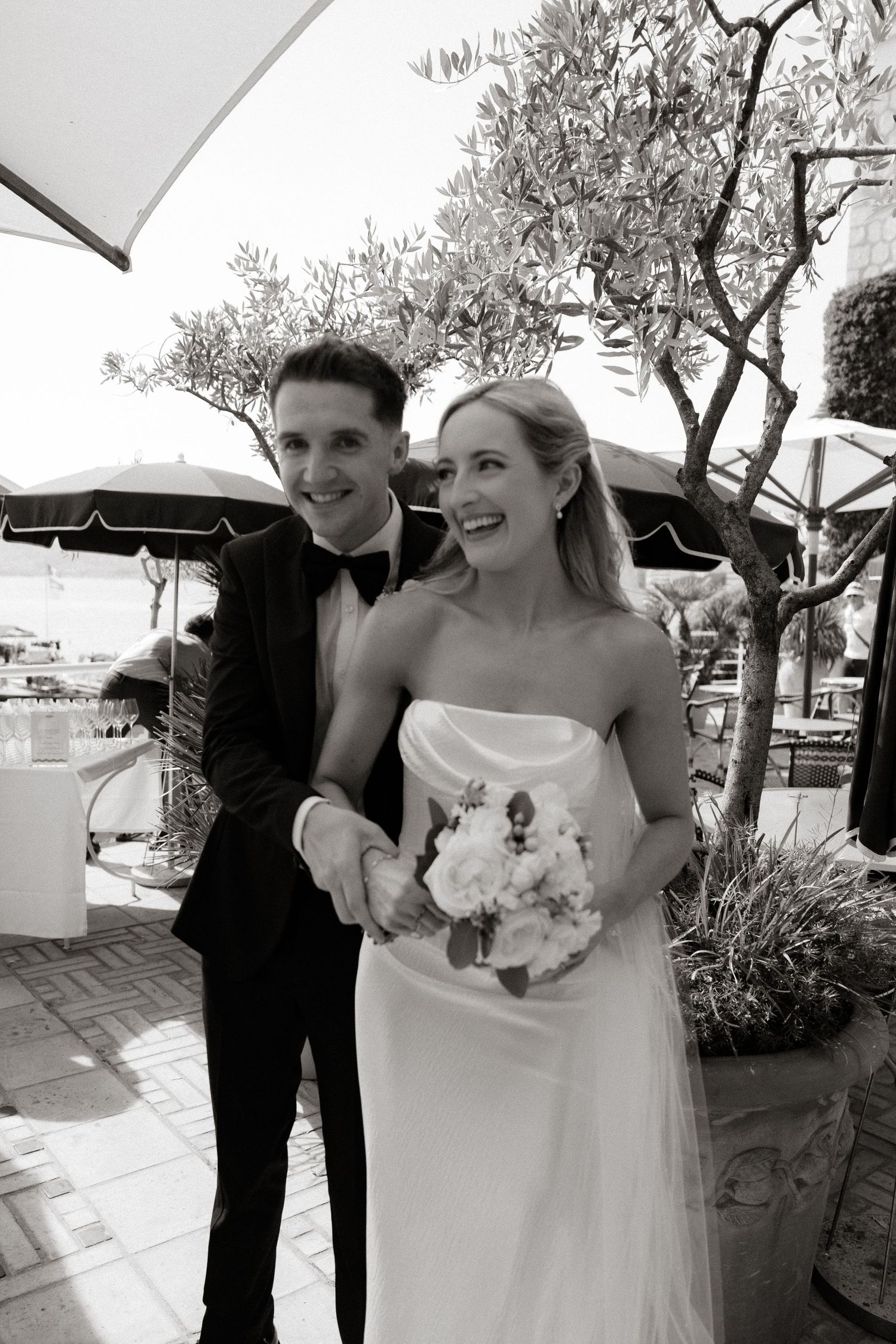 Four progressive black and white wedding photos show a joyful couple laughing and posing outdoors under olive trees.