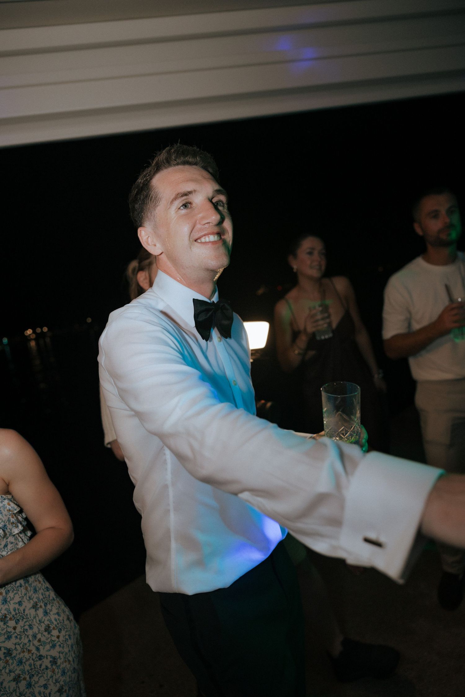 A gentleman in formal attire dances at a wedding reception with a bright blue light in the background.