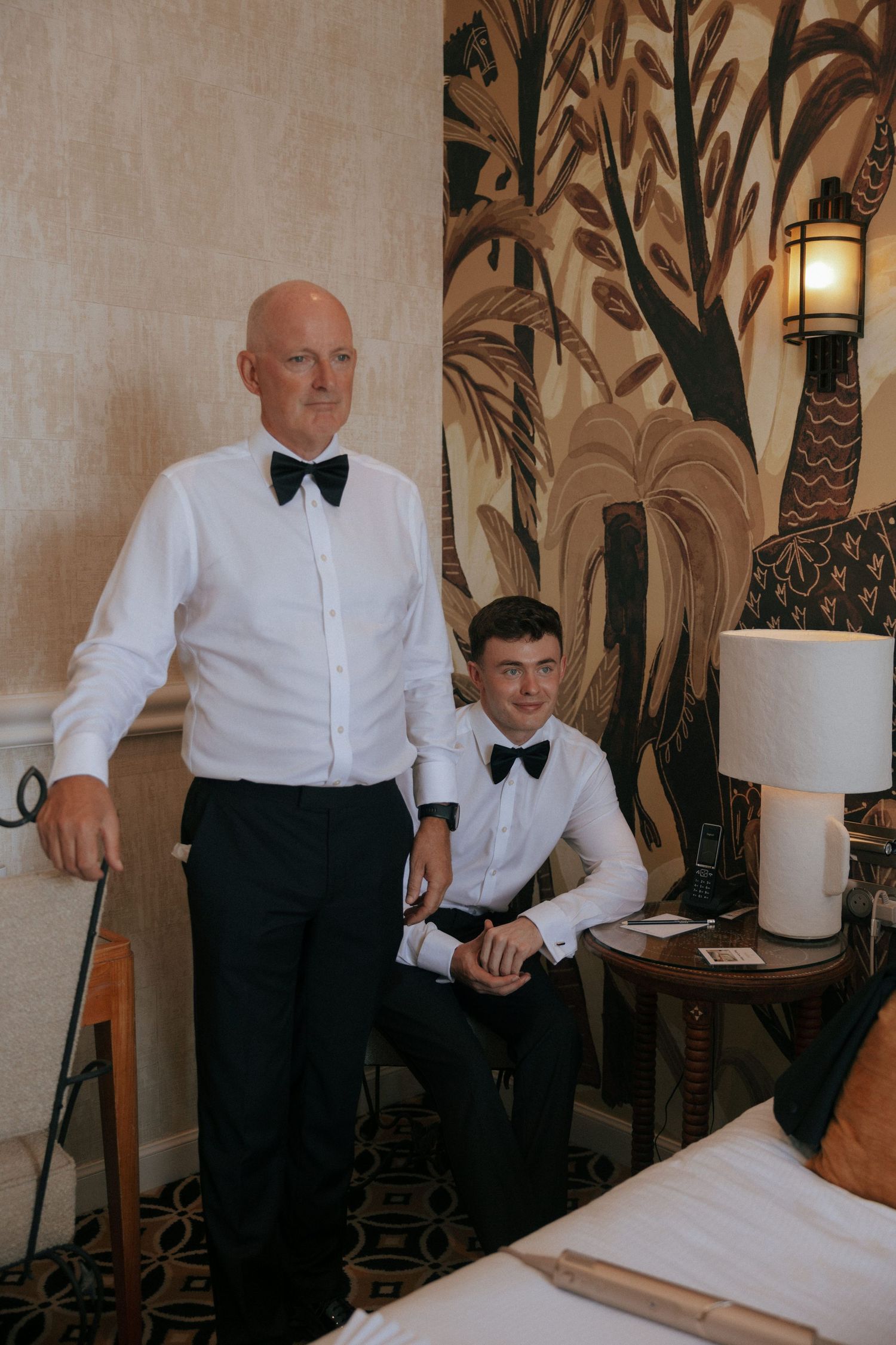 Wedding party members in formal attire getting ready in an elegantly decorated room with tropical wallpaper.