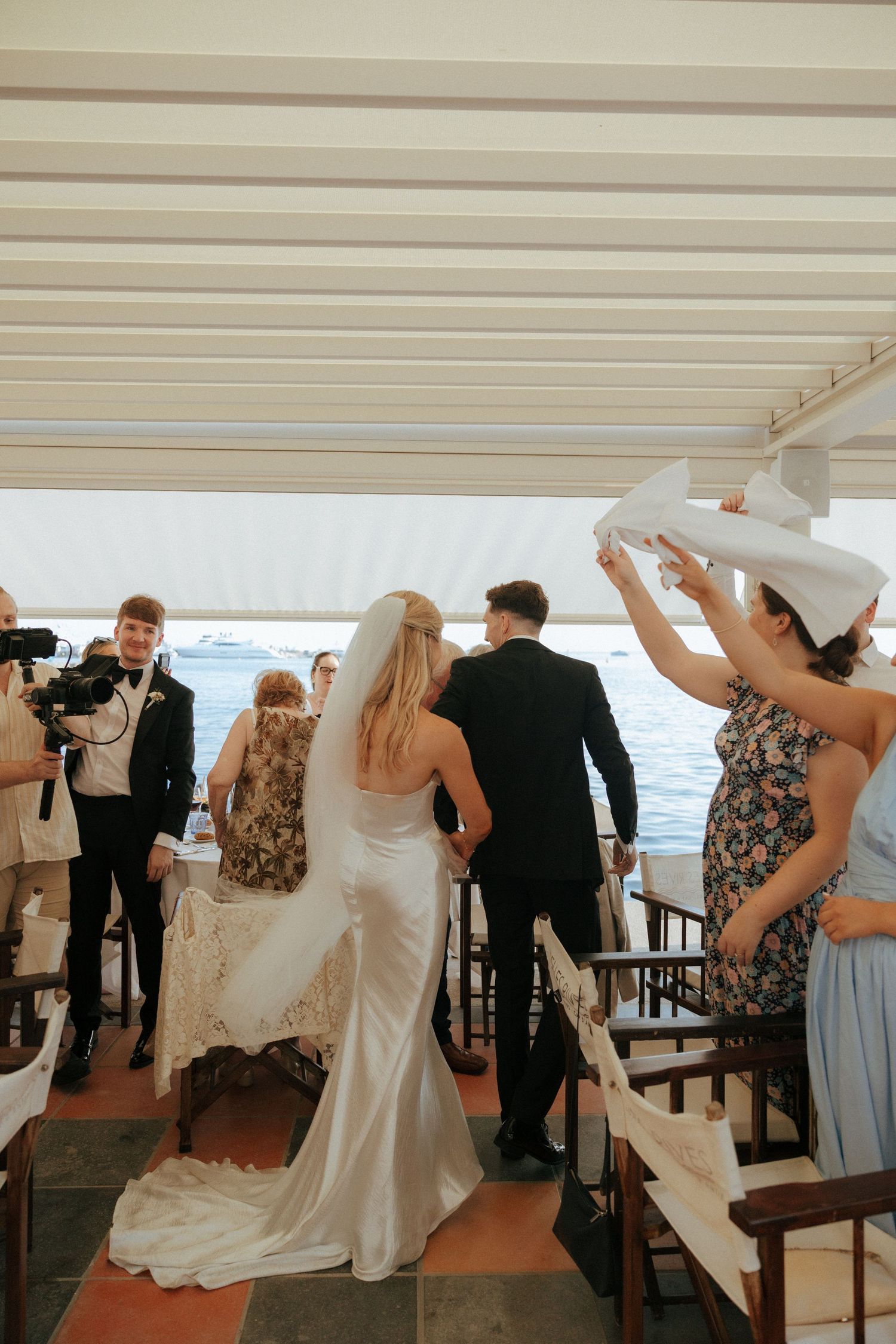 Wedding guests gather on a boat deck during a nautical ceremony with attendees and photographer capturing the moment.