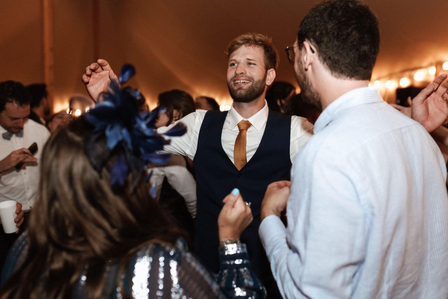 Wedding guests dancing and celebrating at a lively reception under string lights.
