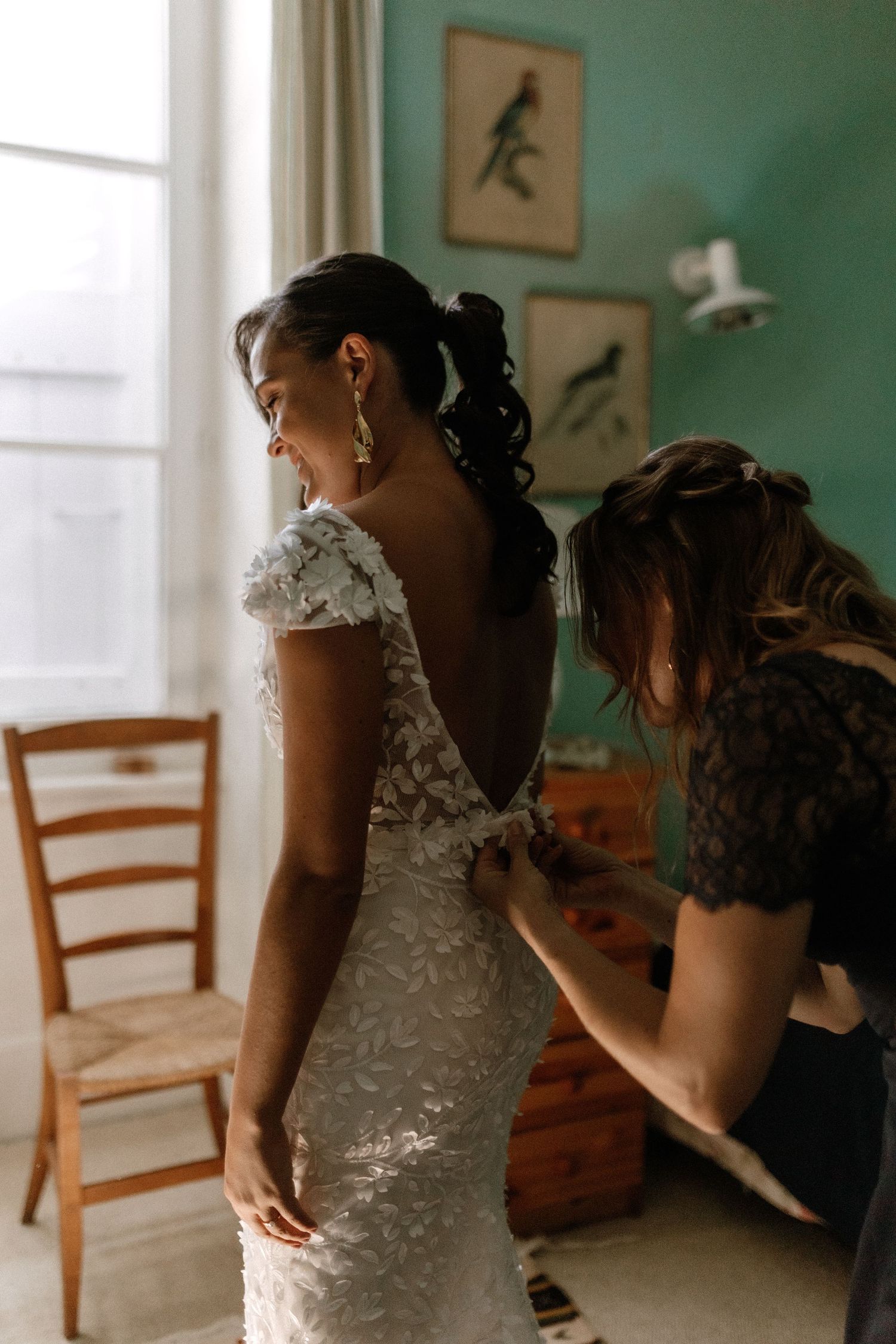 Final wedding dress fitting in a sunlit room with teal walls decorated with bird artwork.