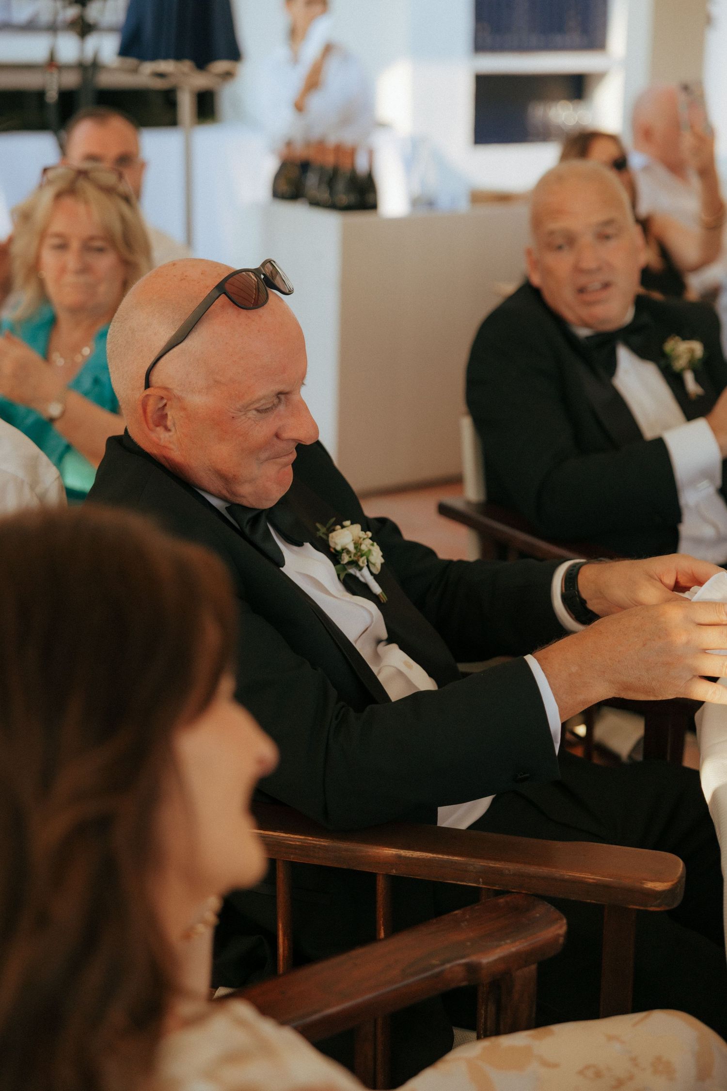 Wedding guests in formal attire seated at reception tables share candid moments together.