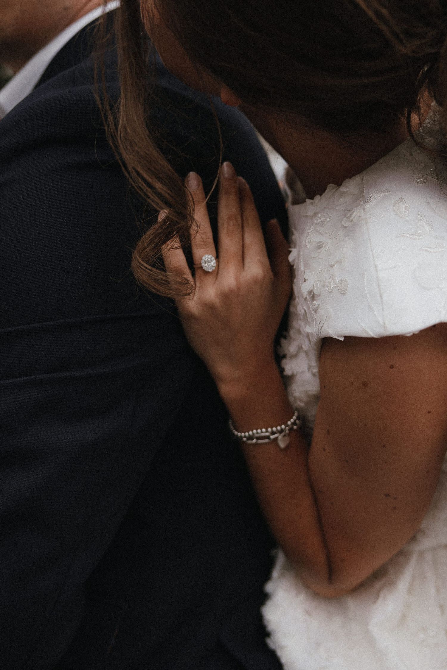 A black and white romantic wedding photo showing a tender embrace in shadow with a diamond ring visible.