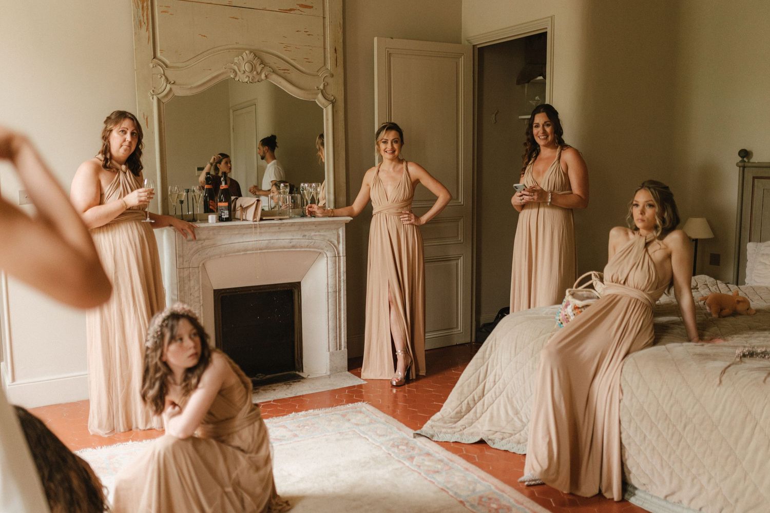 Bridesmaids in blush dresses relaxing in an elegant room with vintage fireplace.