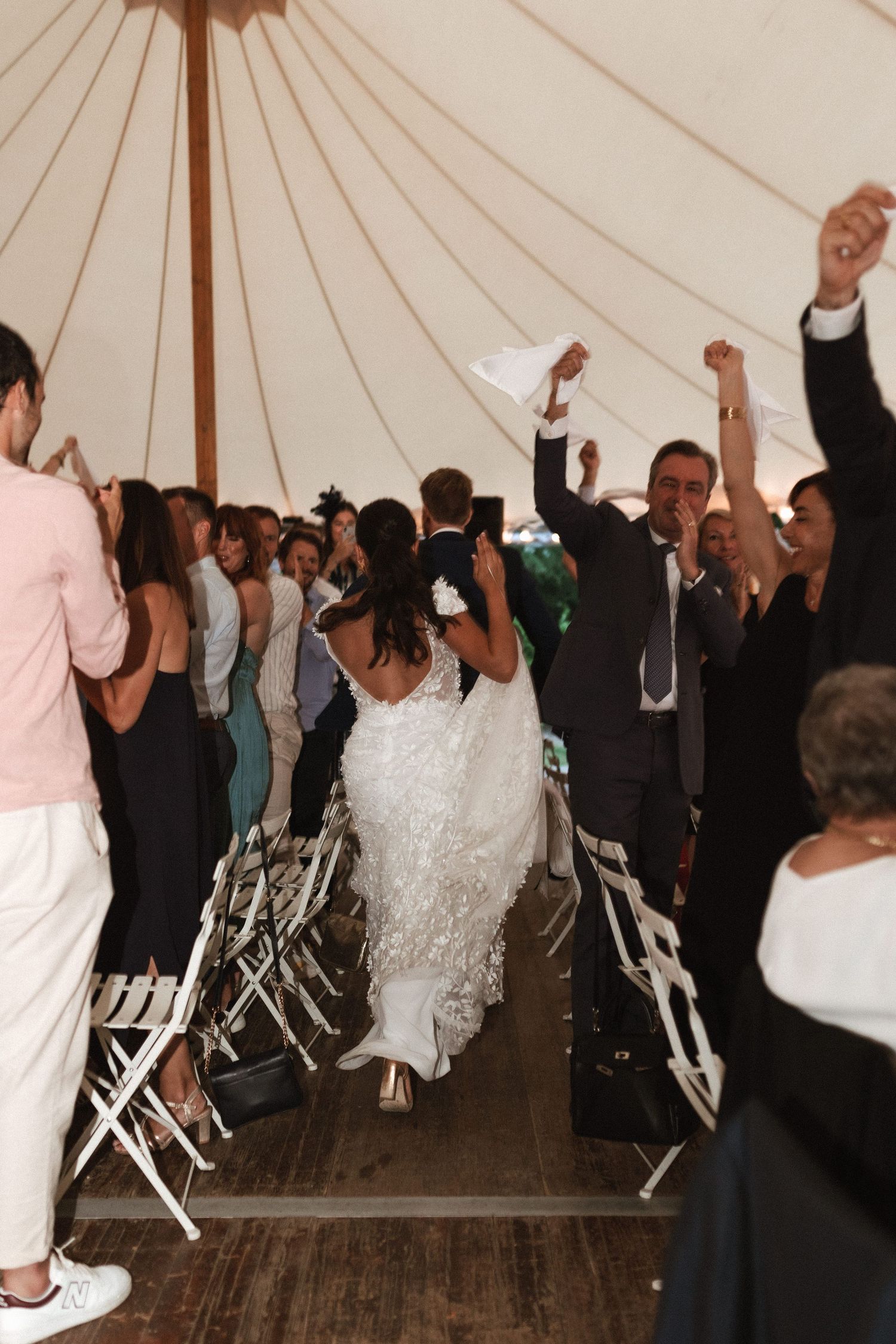 Wedding party celebrating under a white tent with raised arms and dancing.