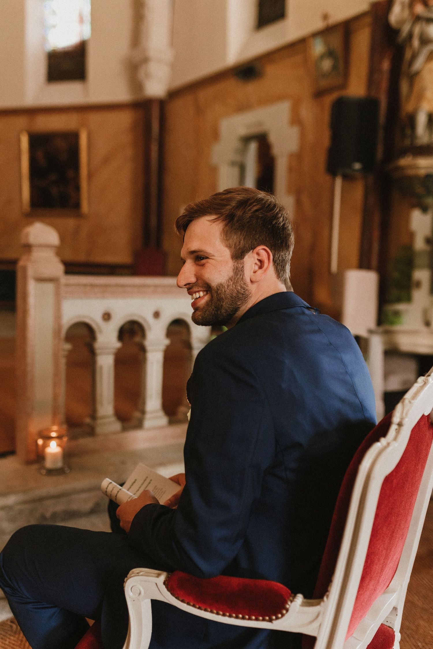Wedding guest seated in an elegant chair smiles in a historic church interior.
