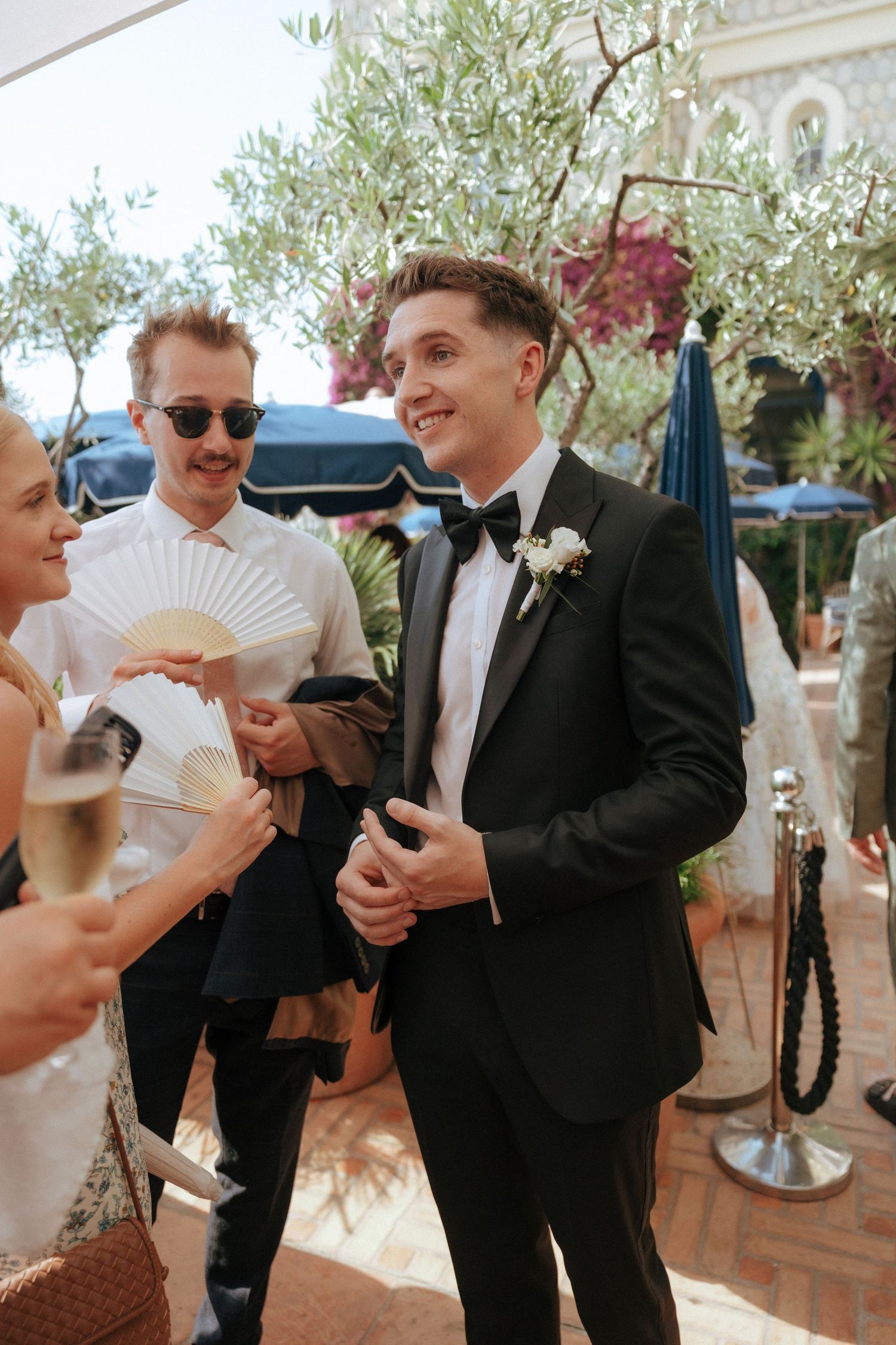 Wedding couple and guests share playful moments with decorative white fans at an outdoor reception.