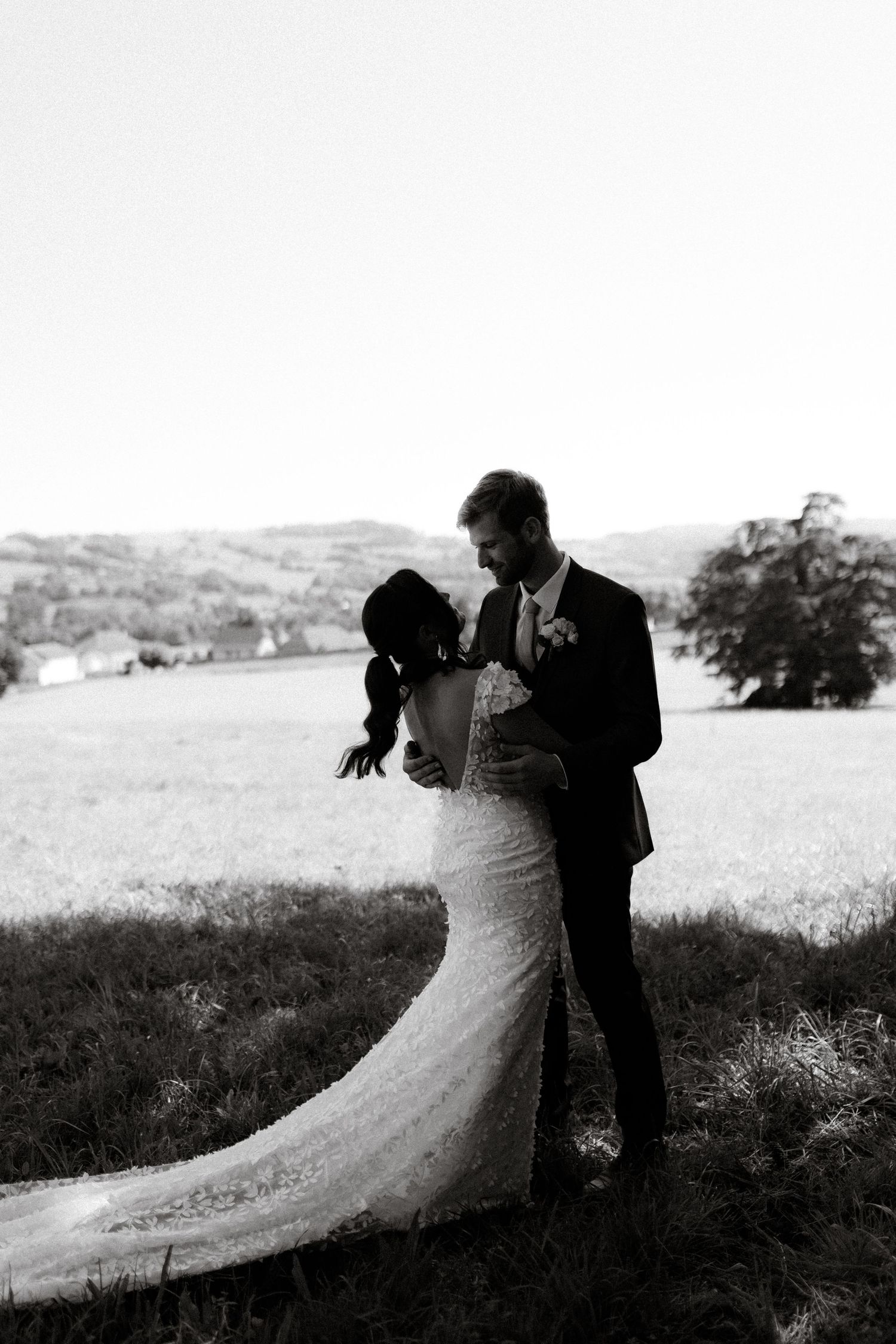Black and white silhouette of newlyweds embracing on a hillside.