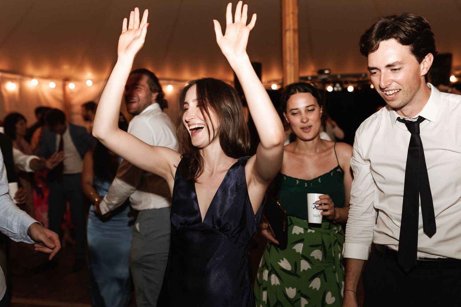 Wedding guests dancing and celebrating with enthusiasm under a tent.