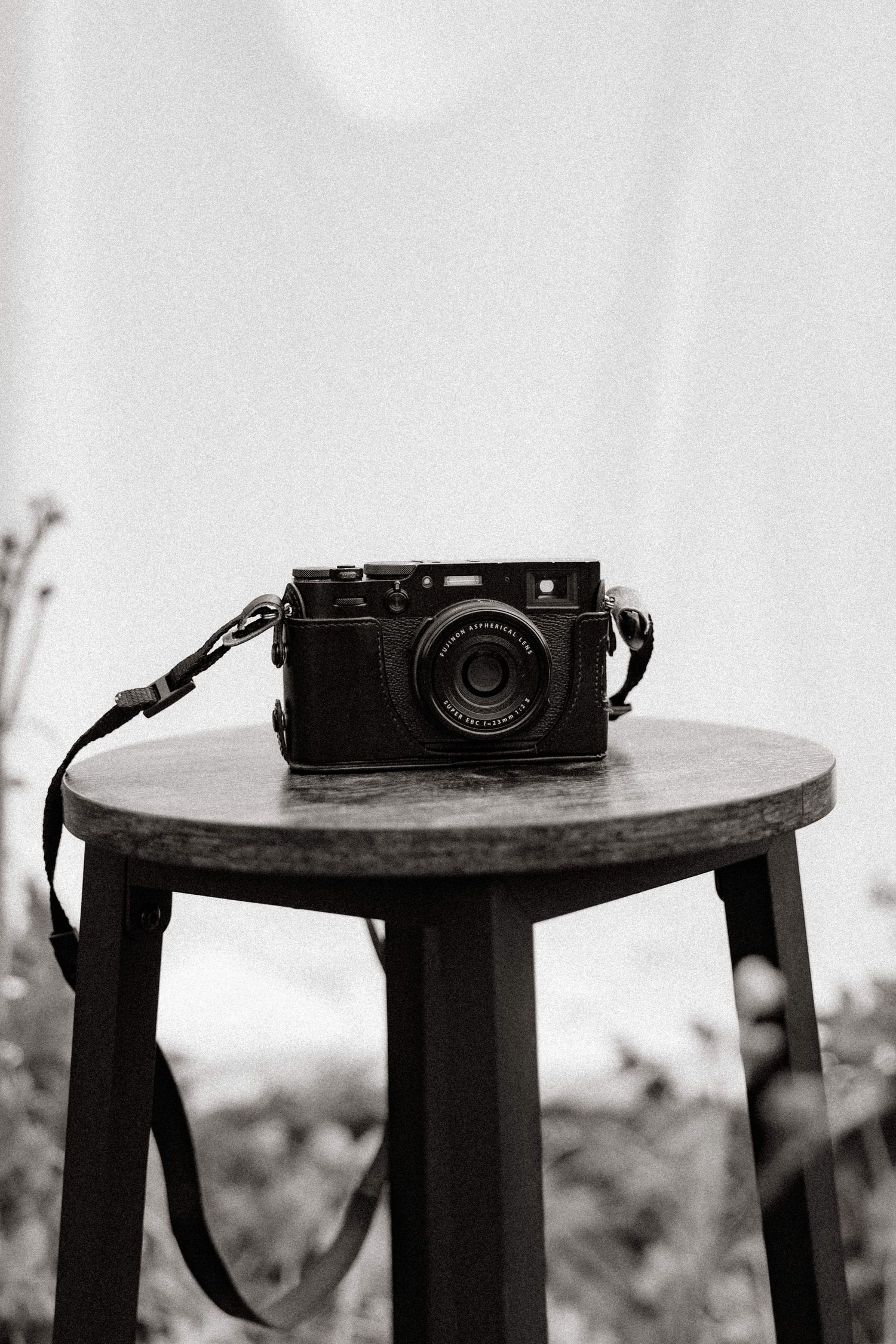 A black and white photo of a vintage camera placed on a wooden stool.