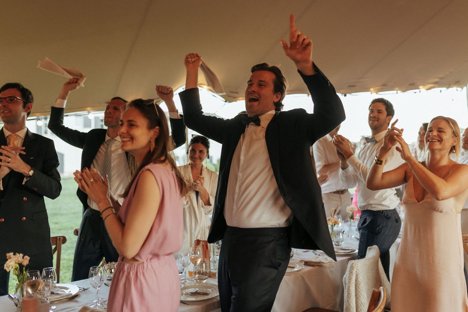 Wedding reception guests dancing and celebrating with raised hands under a white tent.