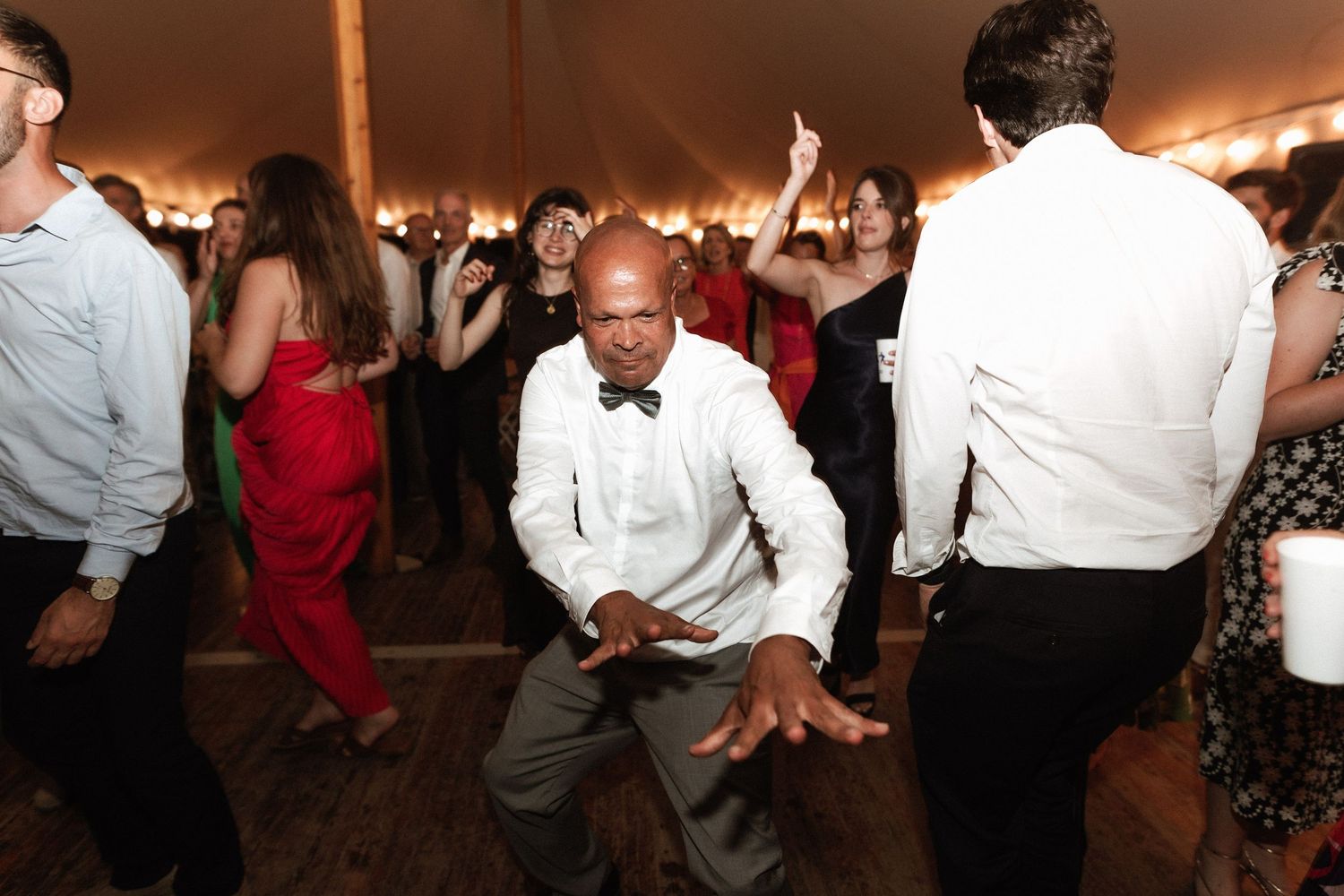 Energetic dancing at a wedding reception under string lights.