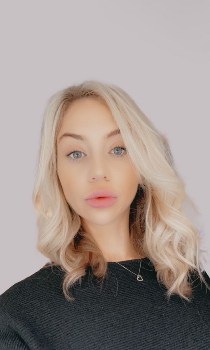 Professional headshot of blonde woman in black sweater against light grey background.