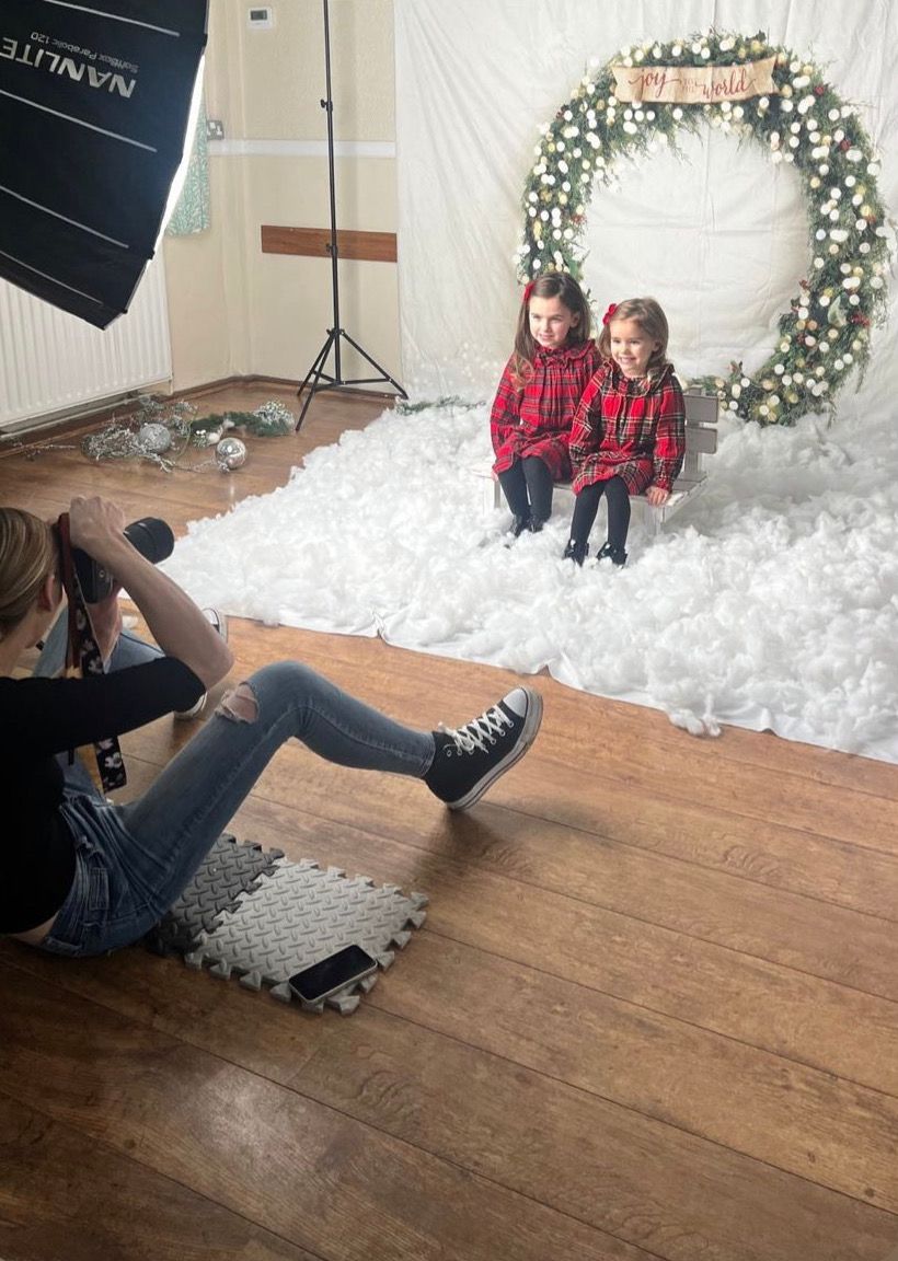 Behind the scenes photo of photographer shooting holiday portraits with snowy backdrop and floral arch.
