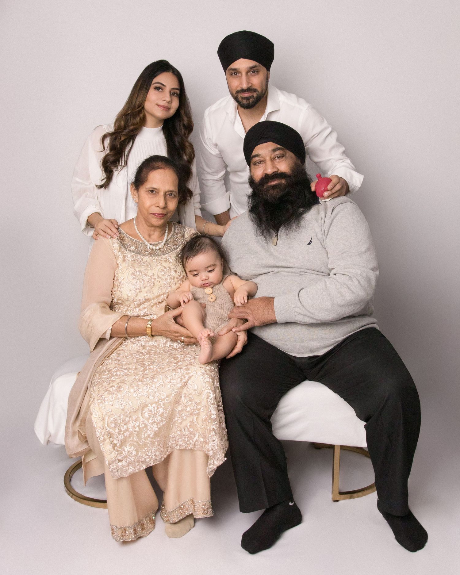 Multi-generational family portrait in coordinated neutral outfits against grey backdrop.
