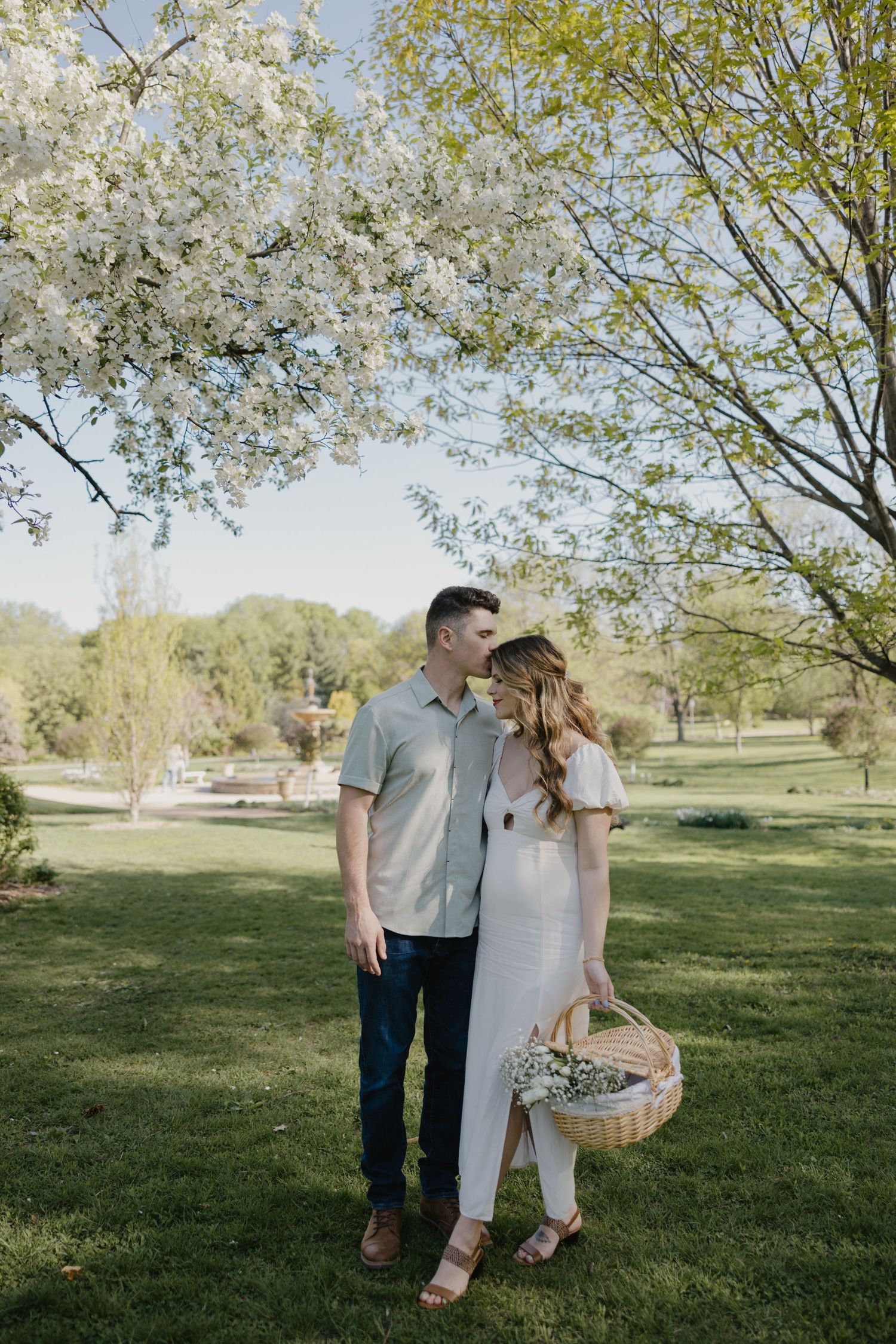 A couple standing under blooming cherry blossoms in a spring garden with a woven basket.