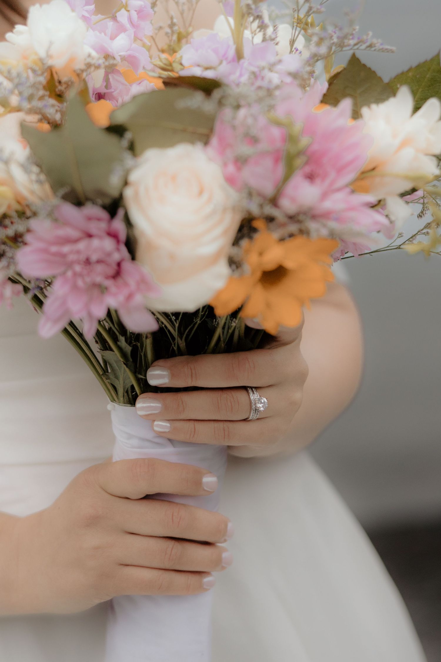 Hands gently holding a delicate pink and white flower arrangement against a soft gray background.