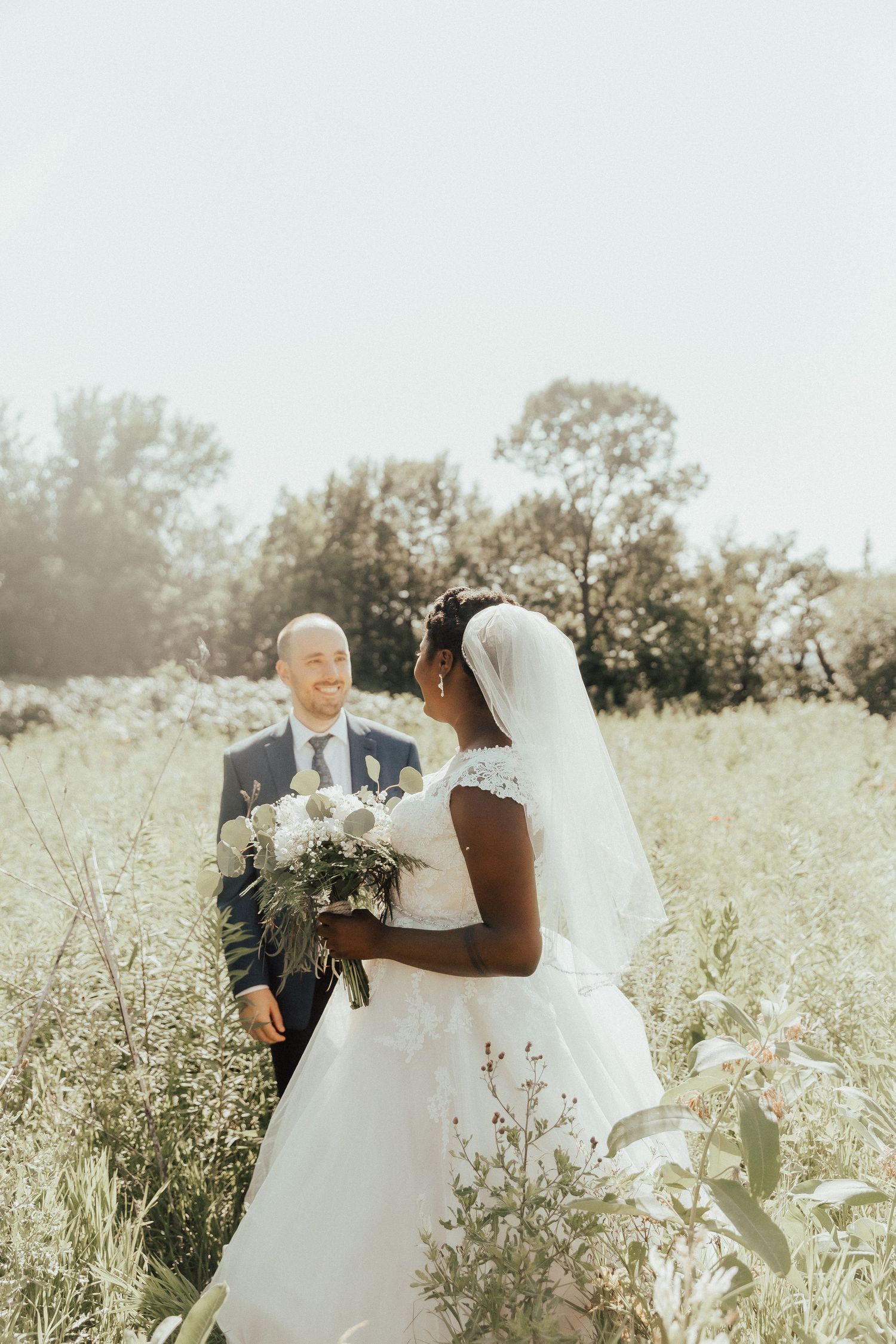 Romantic outdoor wedding portrait in a sunlit meadow with wildflowers.