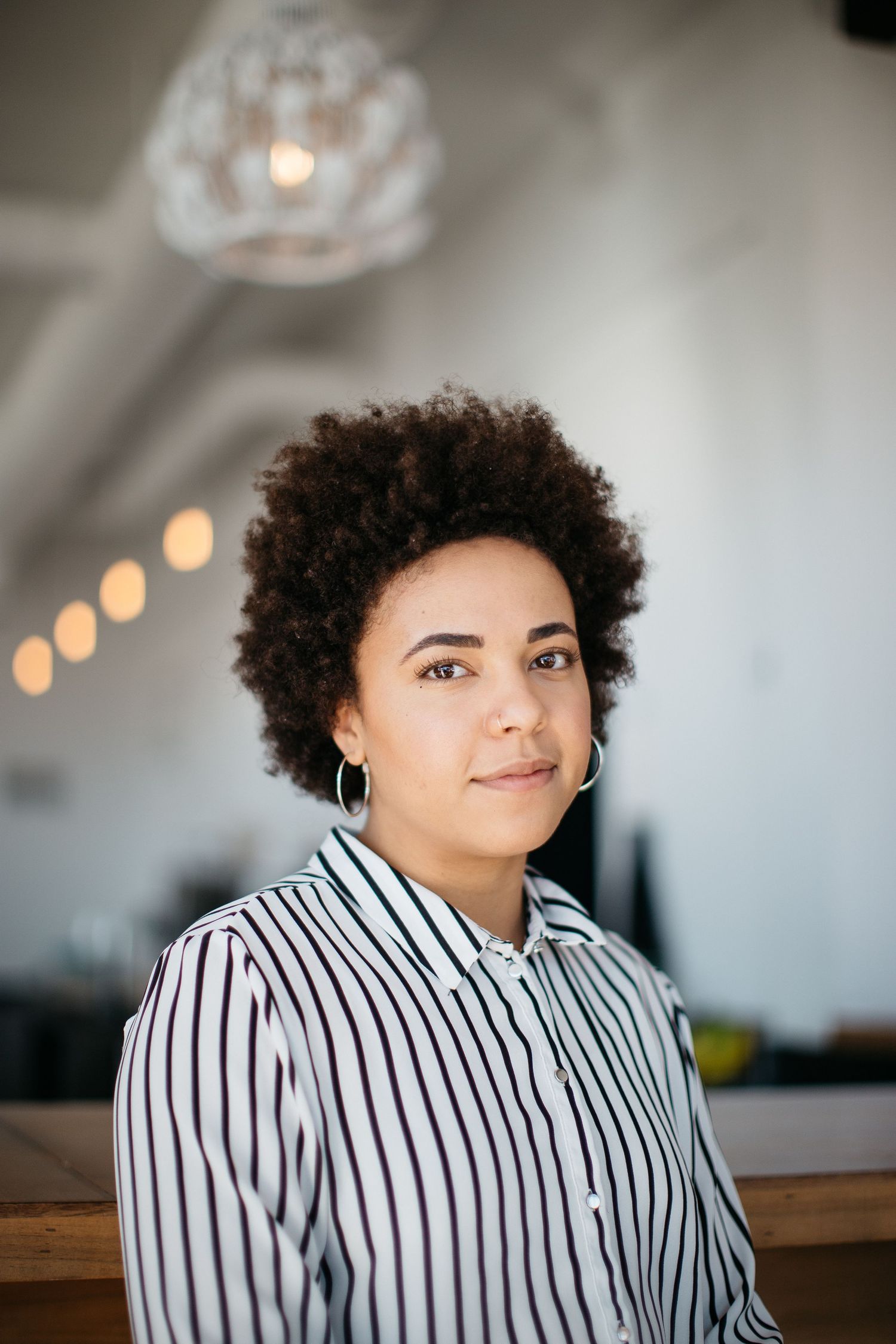 Professional portrait of person in striped shirt with natural hair against blurred background with warm lighting.