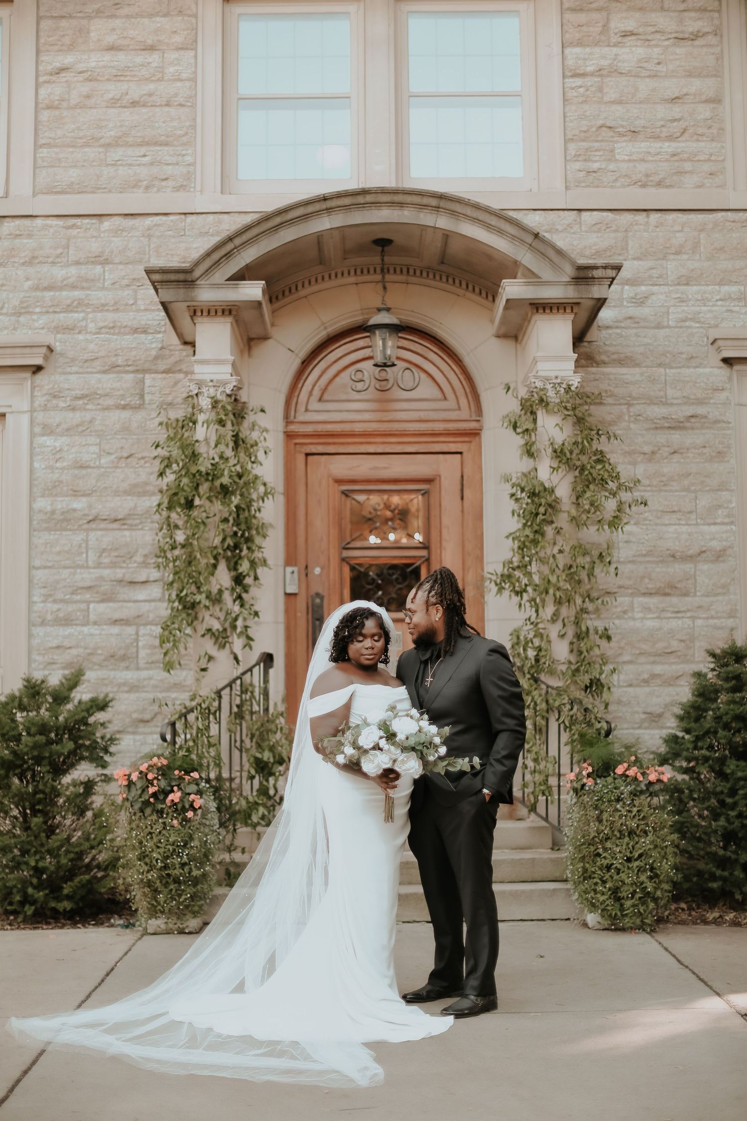Elegant wedding couple posing in front of stone building with arched doorway and climbing vines.