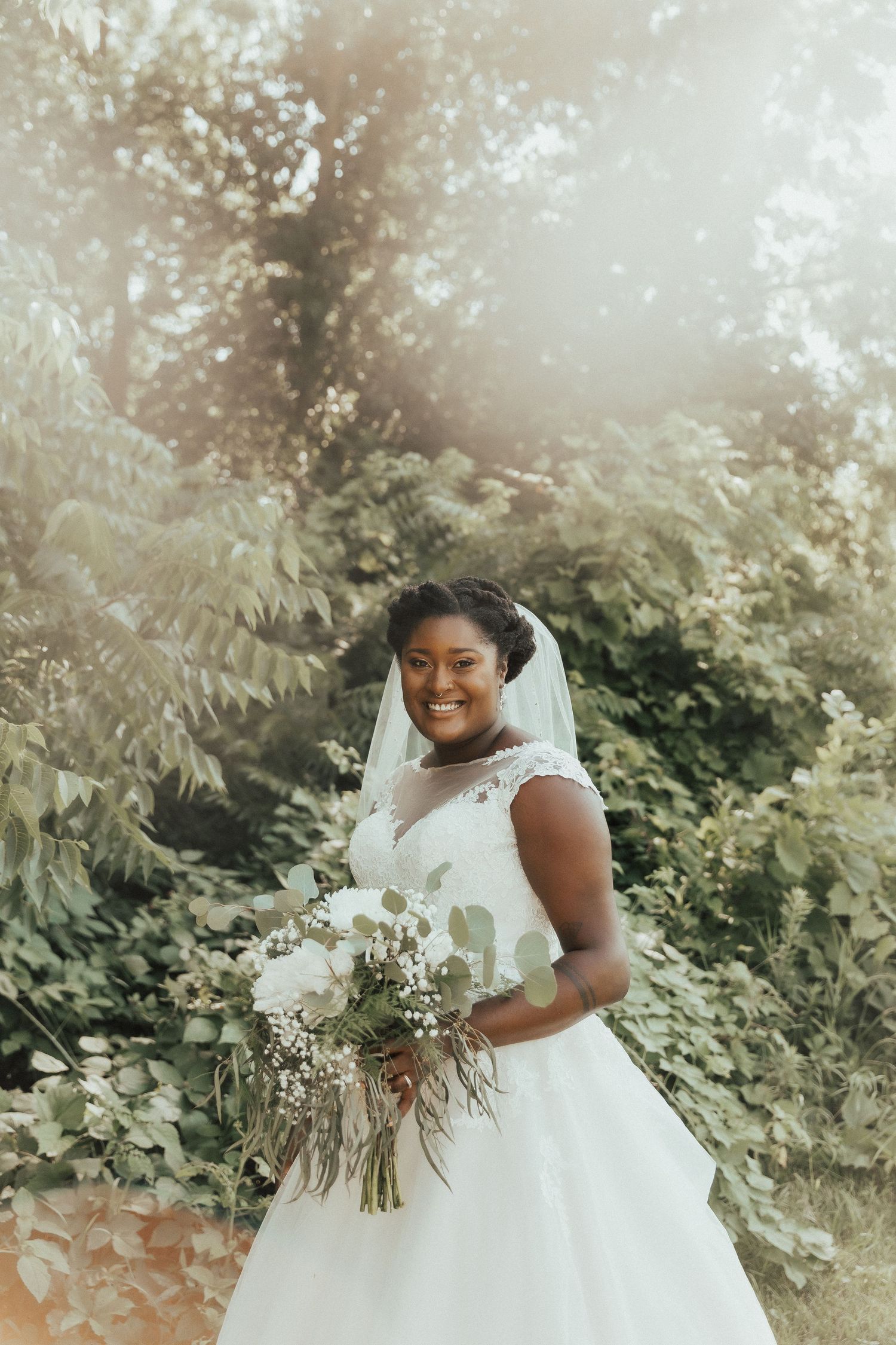 A person in a white wedding gown holds a delicate bouquet of white flowers in a sunlit outdoor setting.